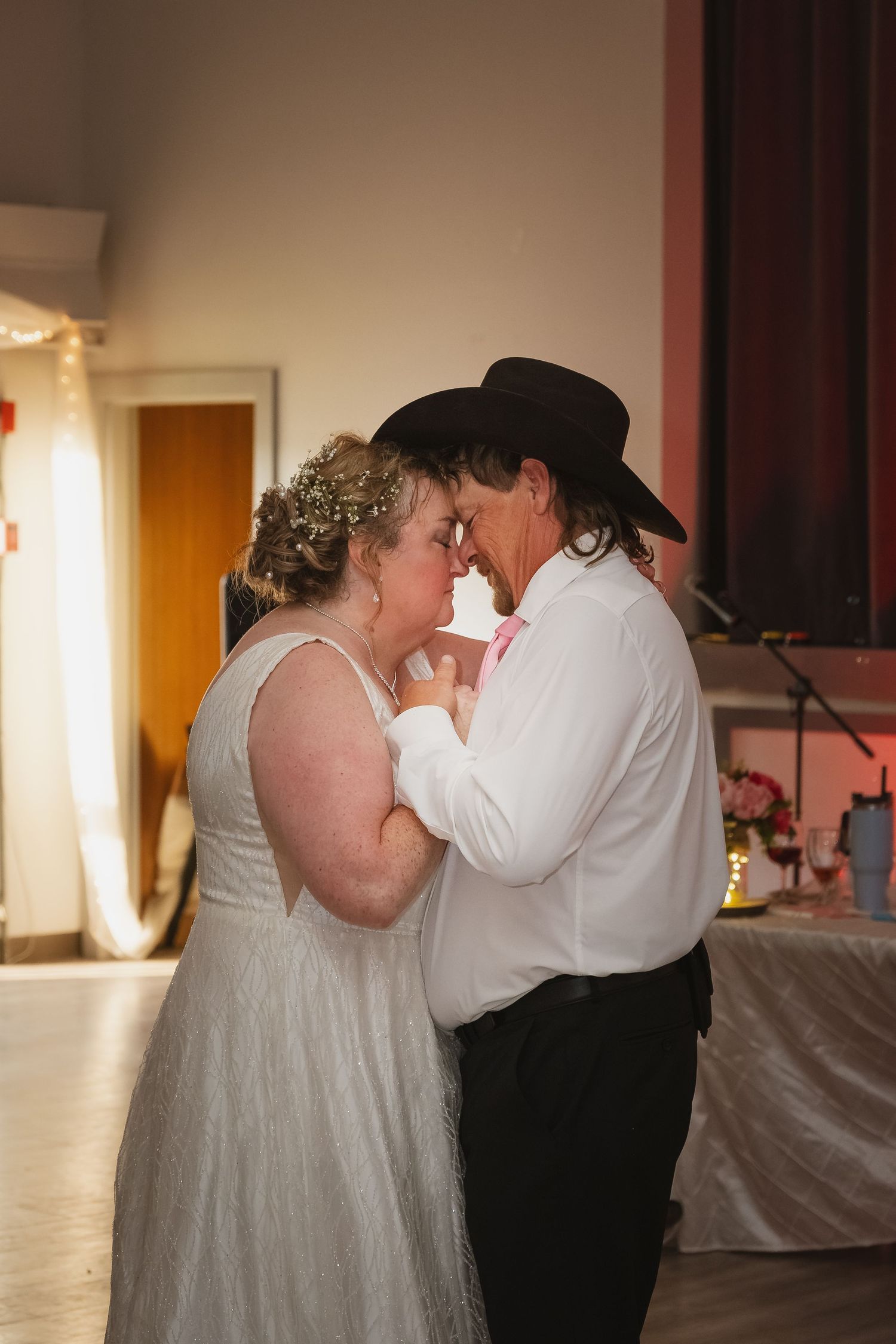 Bride and groom share an intimate first dance, groom wearing black cowboy hat at wedding reception.