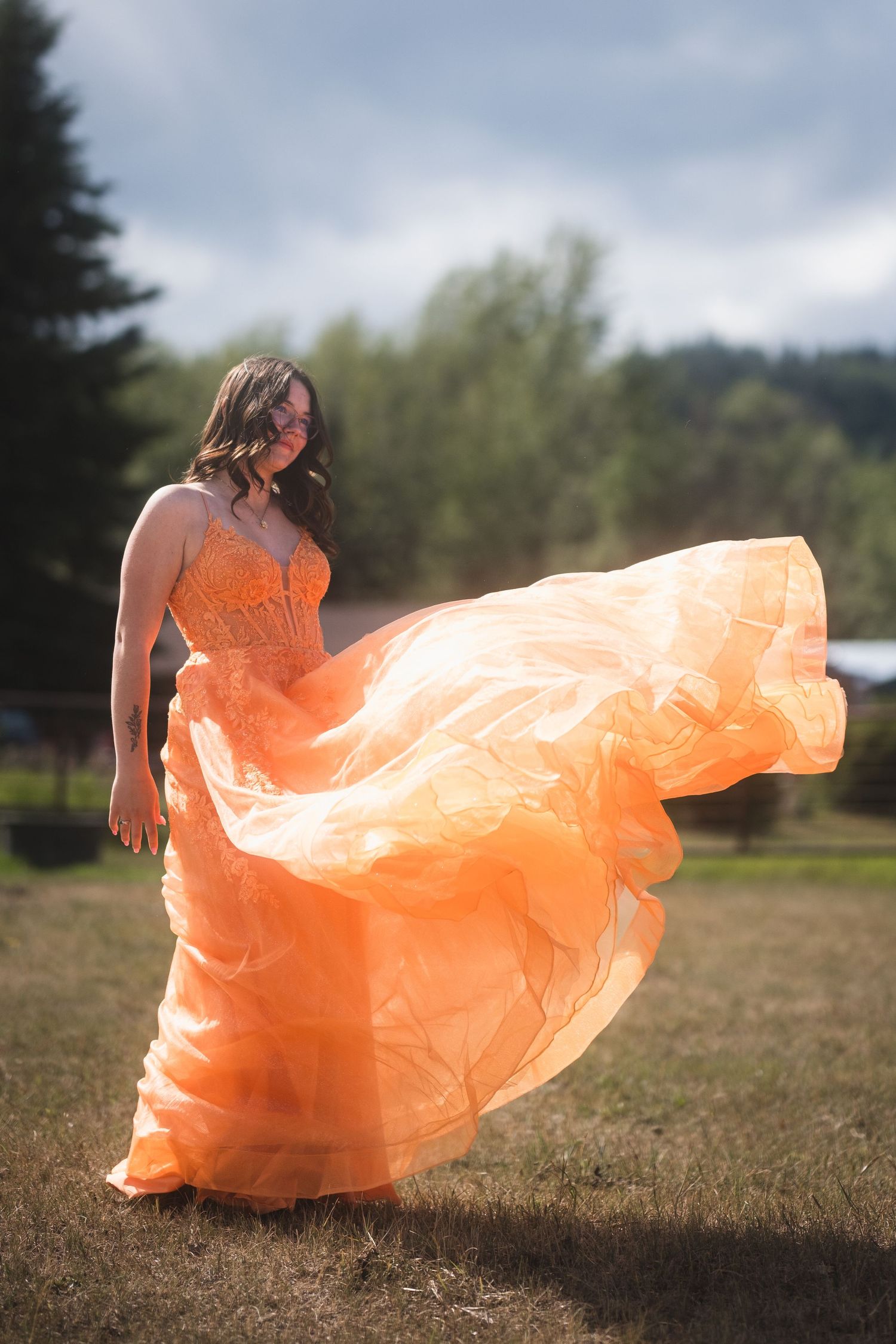 Woman in flowing orange gown twirls as fabric billows dramatically in outdoor field.