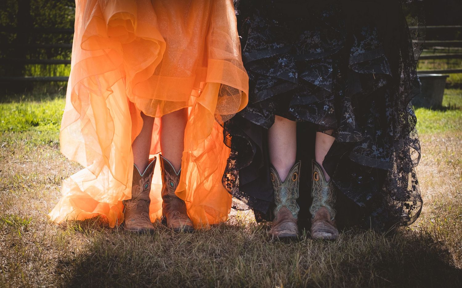 Close-up of two women in formal gowns wearing cowboy boots on grass.