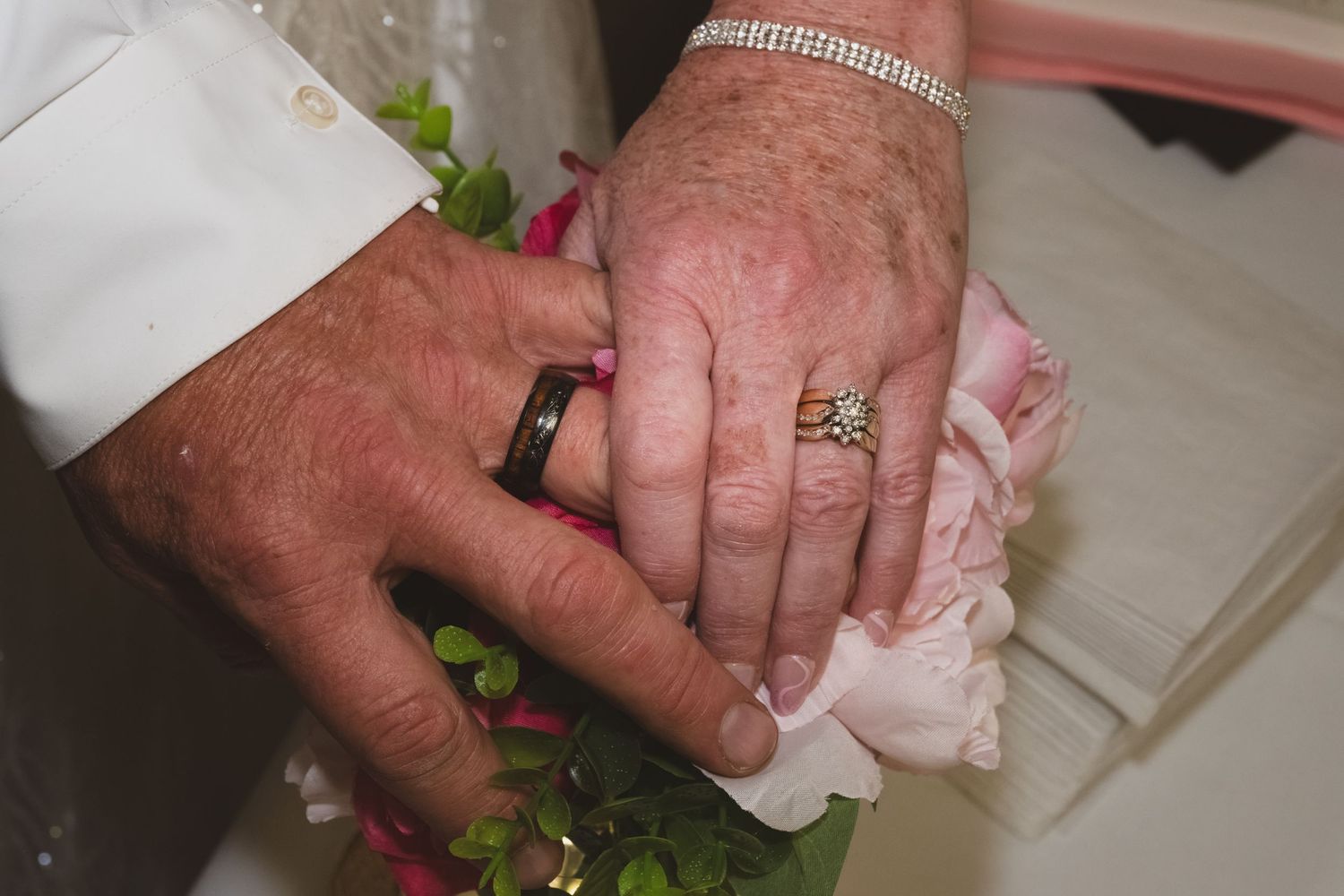 Newlyweds display wedding rings resting on a pink rose bridal bouquet.