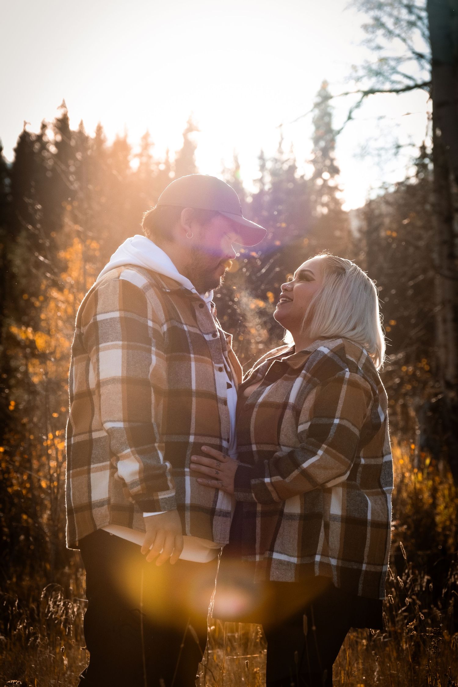 A couple in matching plaid jackets share a romantic moment in a sunlit autumn forest.