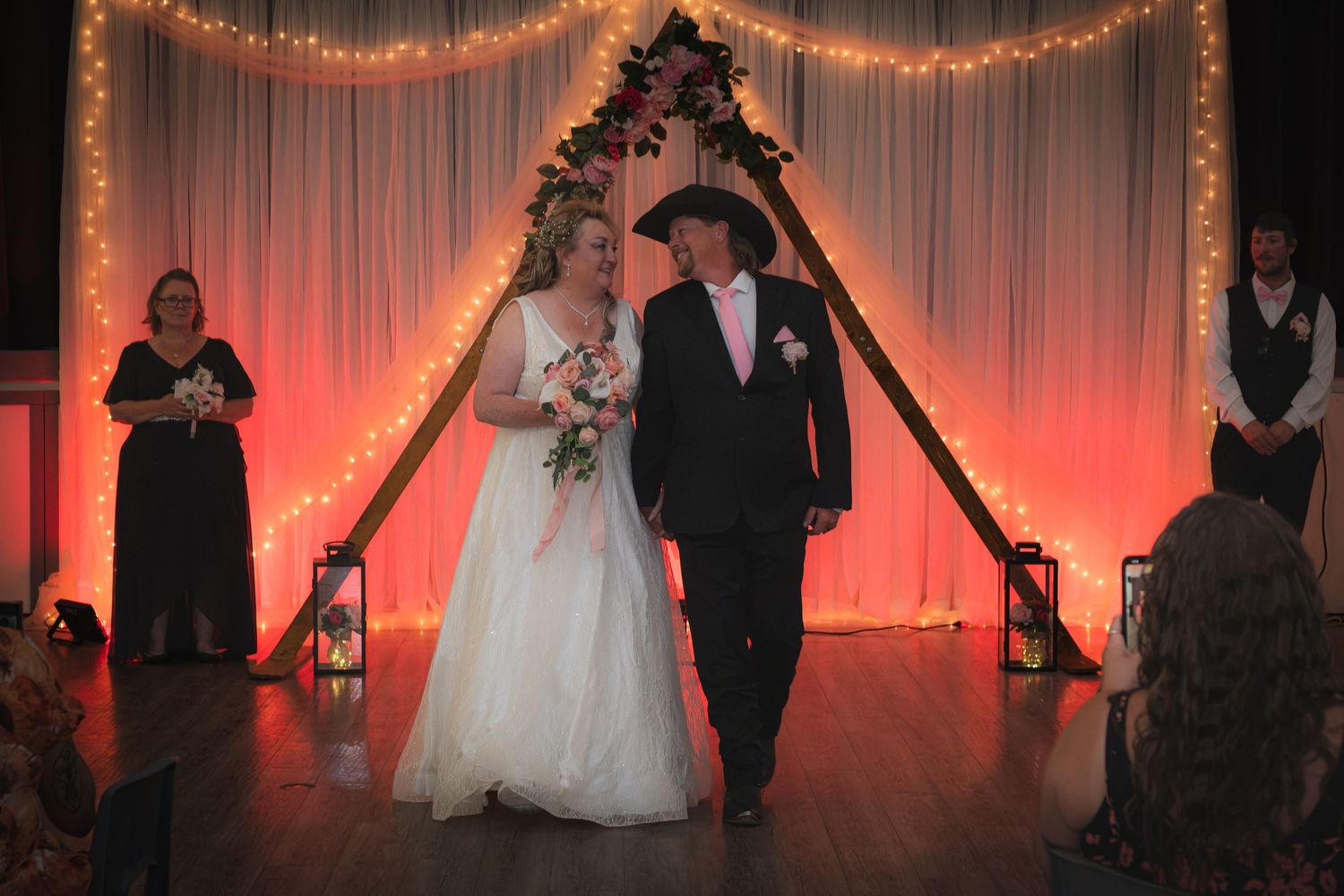 Bride and groom walking down aisle at wedding ceremony with floral arch.