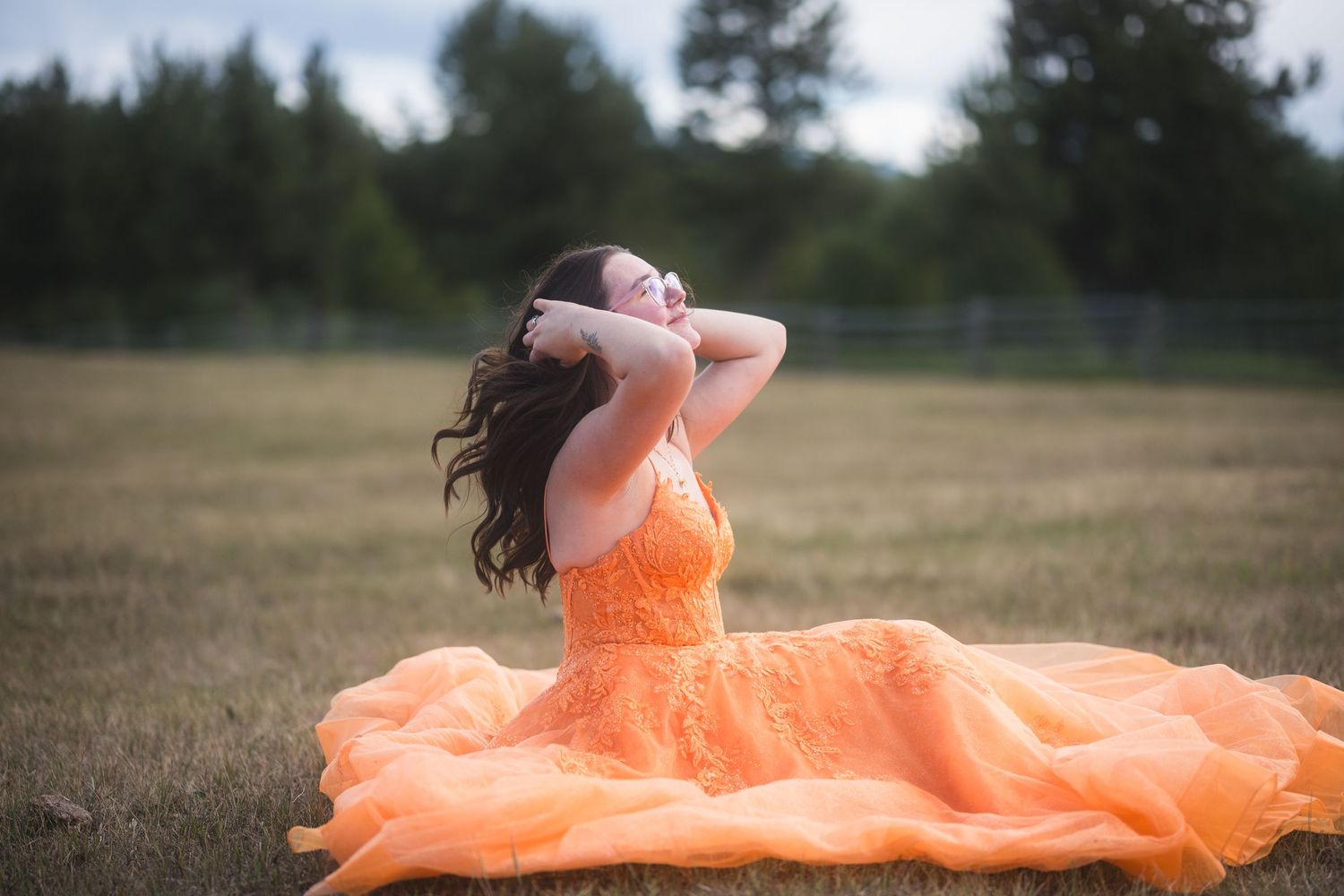Young woman in orange gown sitting in field with hands behind head.
