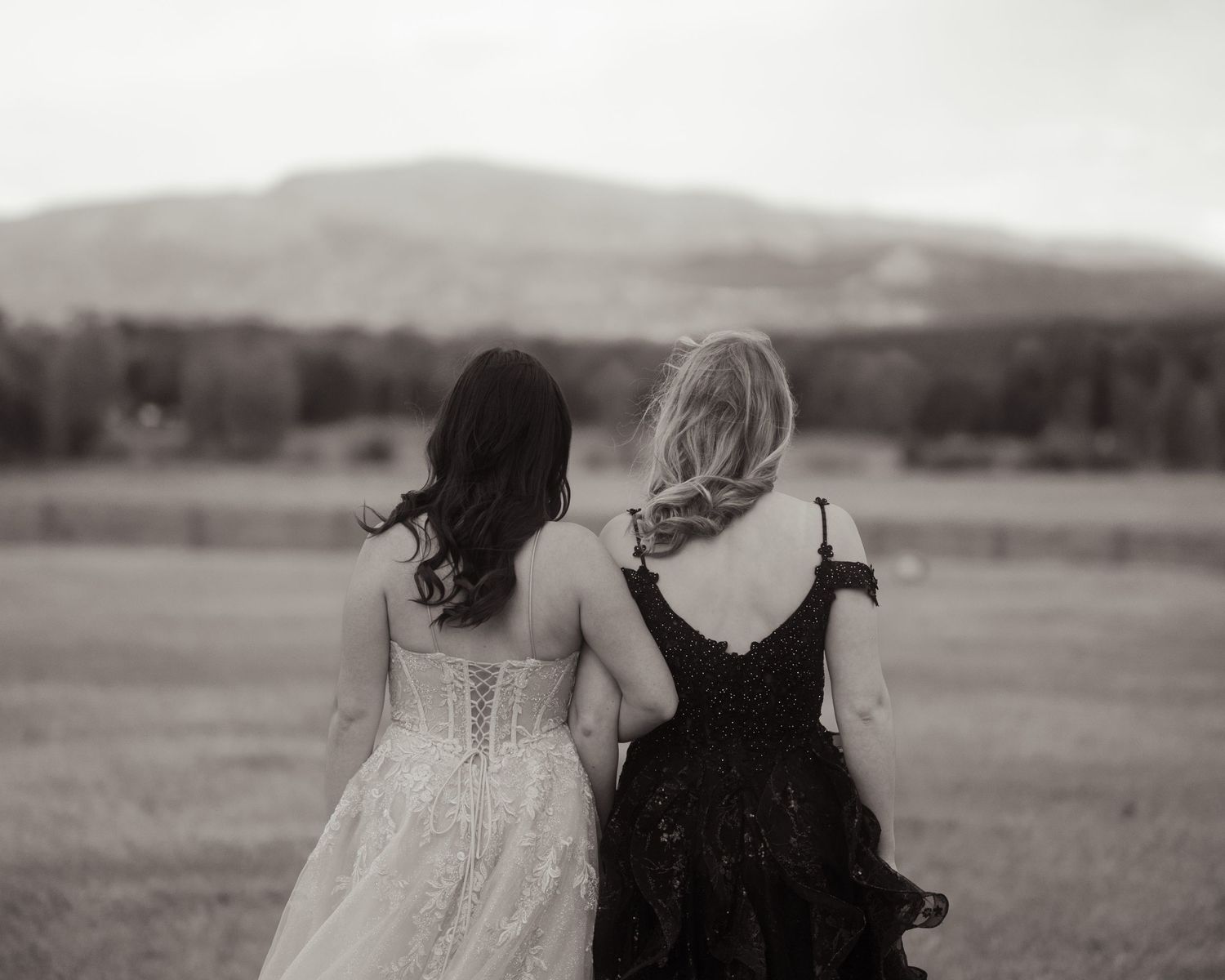 Black and white photo of two women in formal gowns walking toward misty mountain.