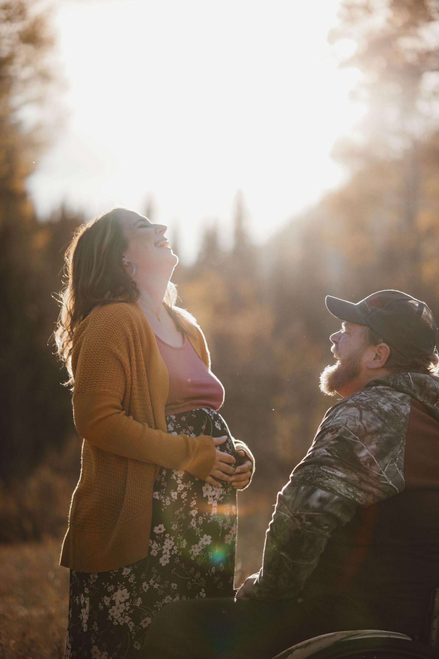 Pregnant woman laughing with bearded man in wheelchair in warm autumn sunlight outdoors.