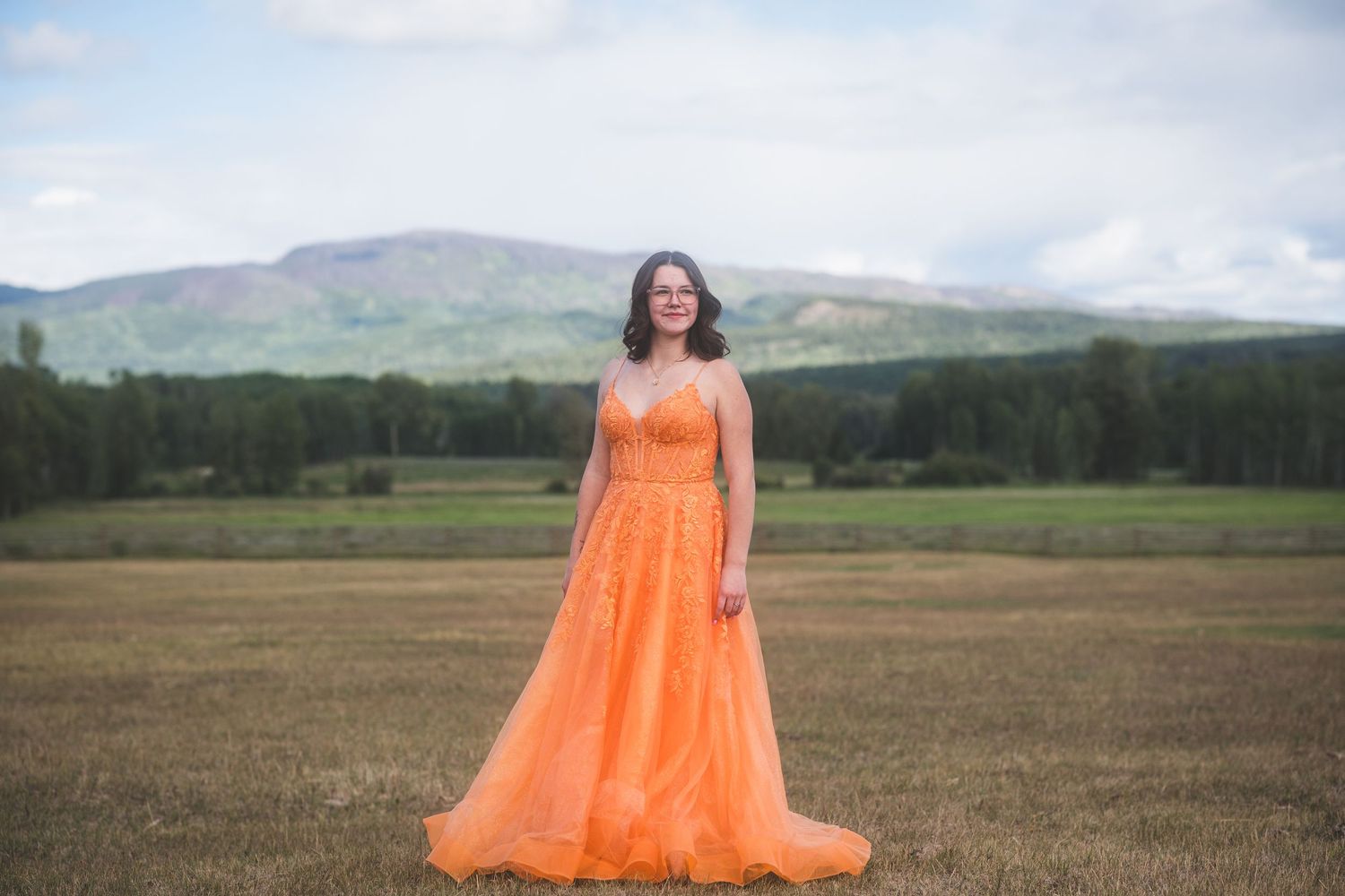 Woman in orange tulle gown standing in field with mountain backdrop.