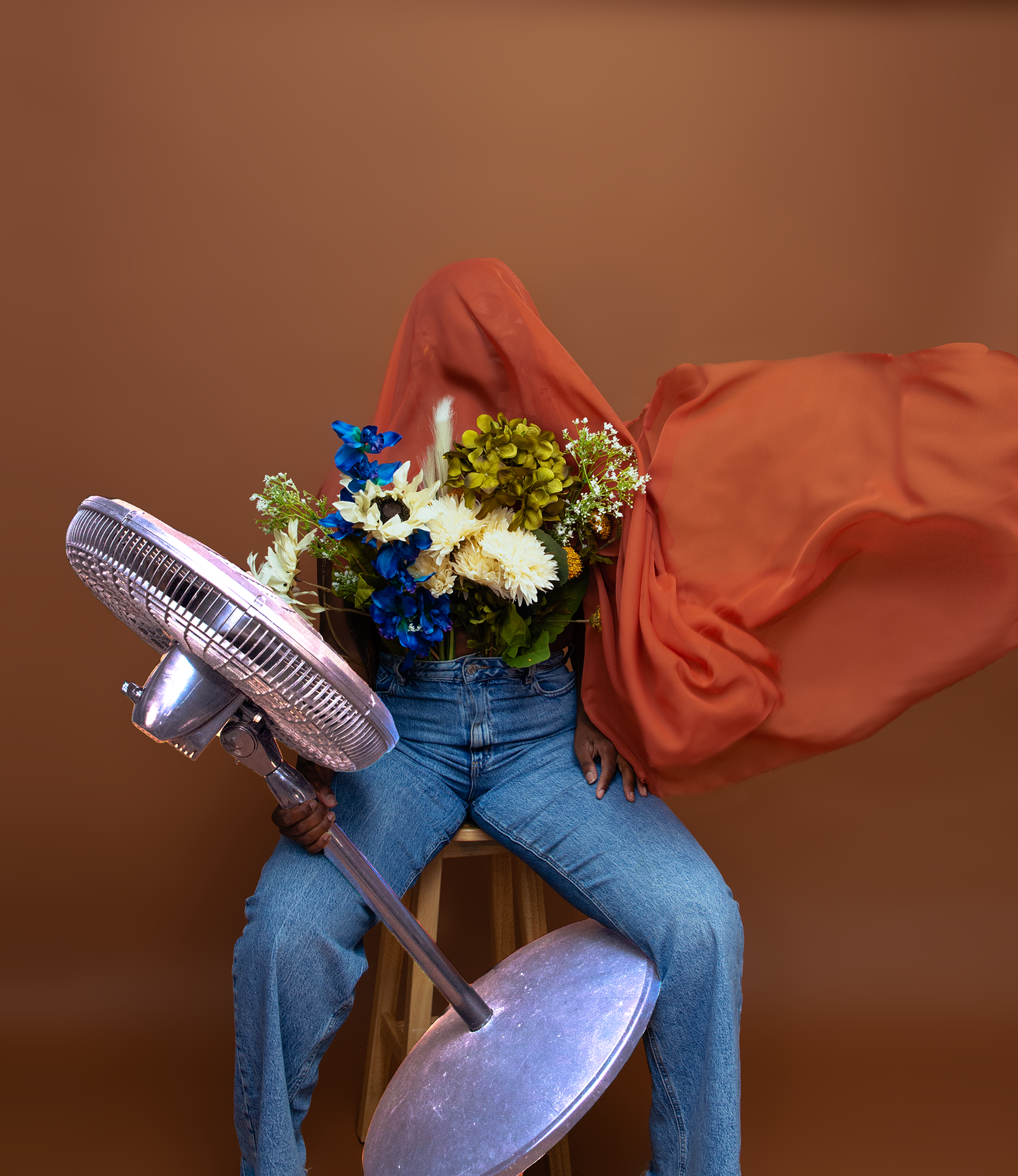 a girl sitting on a chair with a fan and flowers with fabric flowing in the air.