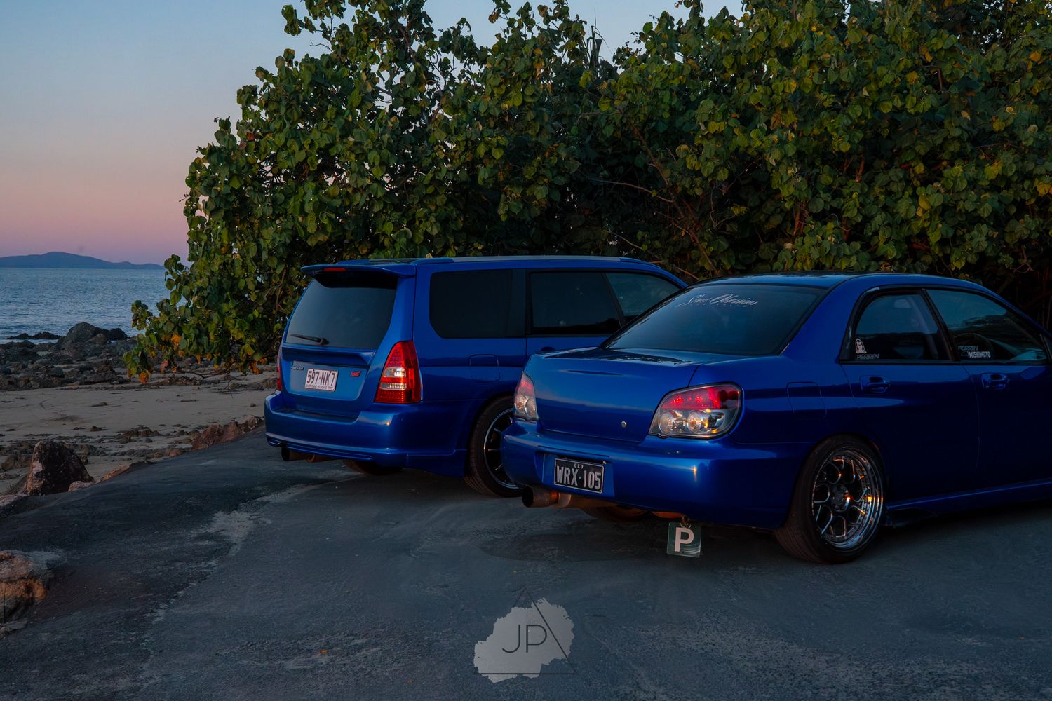 Three blue modified sports cars parked at sunset with mountains and trees in the background.