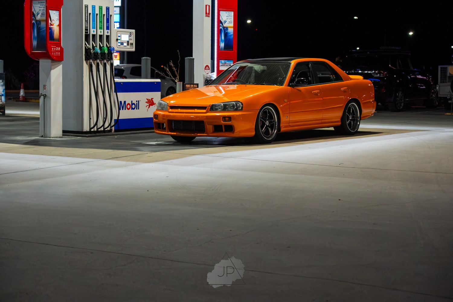 Orange BMW M3 E46 sports car parked in a dimly lit garage space with dark background.