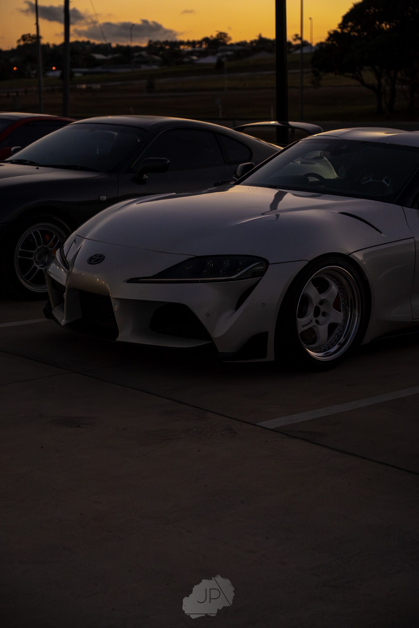 Silhouettes of sports cars parked against a dramatic orange sunset sky.