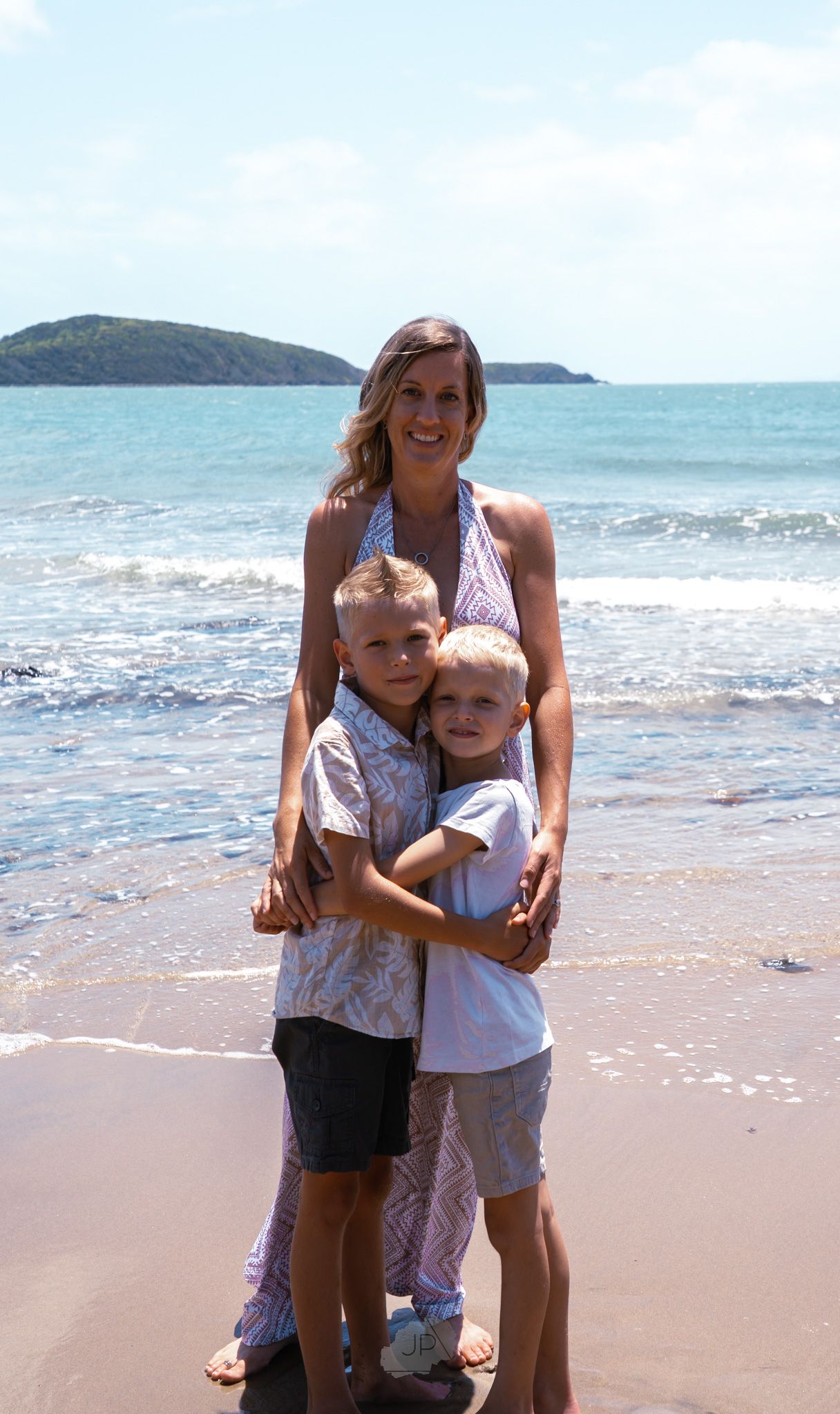 A heartwarming beach scene with family members embracing on the sandy shoreline with ocean waves in the background.