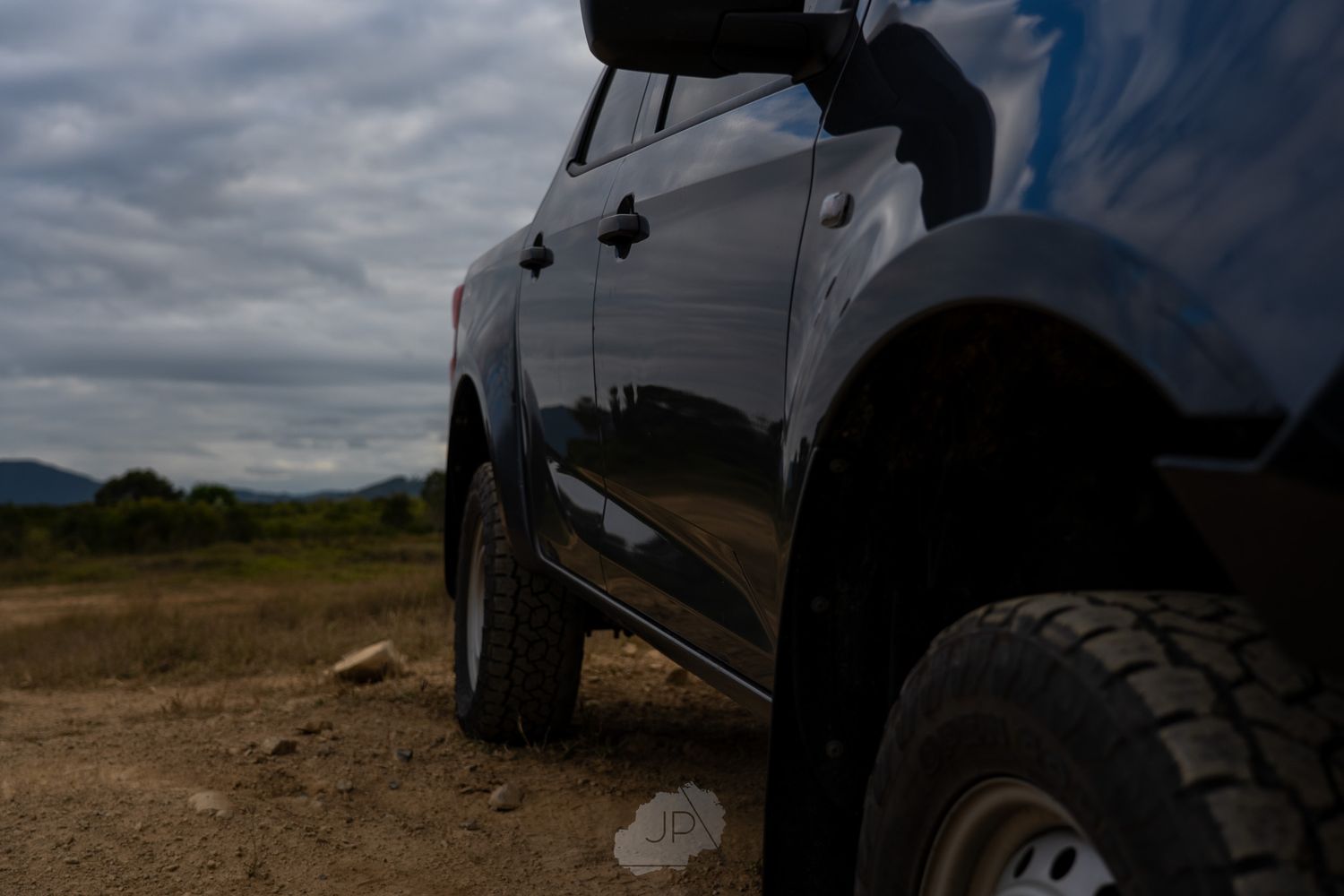 Black pickup truck sitting on rough terrain with large off-road tires under cloudy skies.