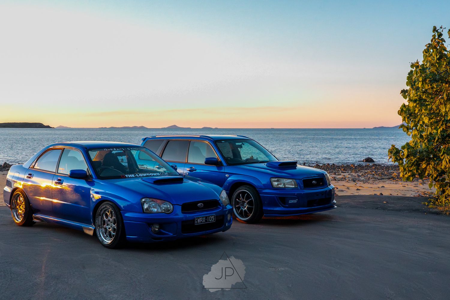 World rally blue Subaru cars lined up along a scenic coastal road during sunset.