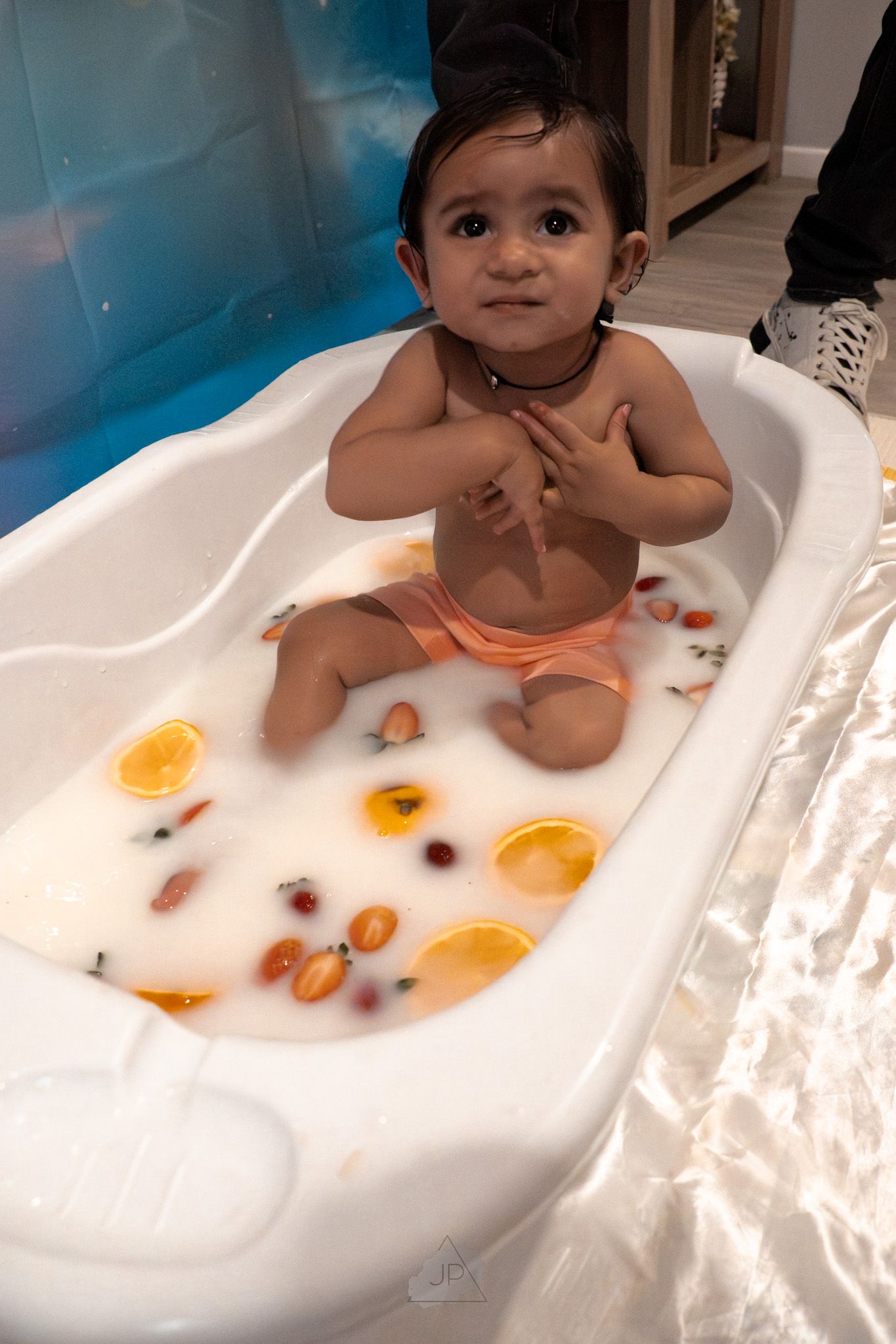 A small child enjoys bath time in a white tub with orange and dark-colored bath toys floating in the water.