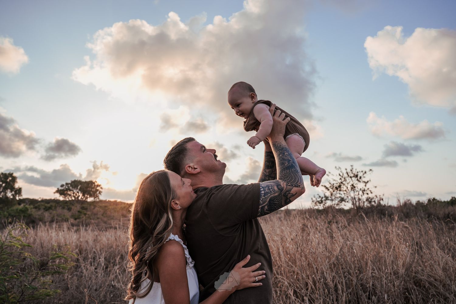 A family shares a tender moment together in a golden field at sunset.