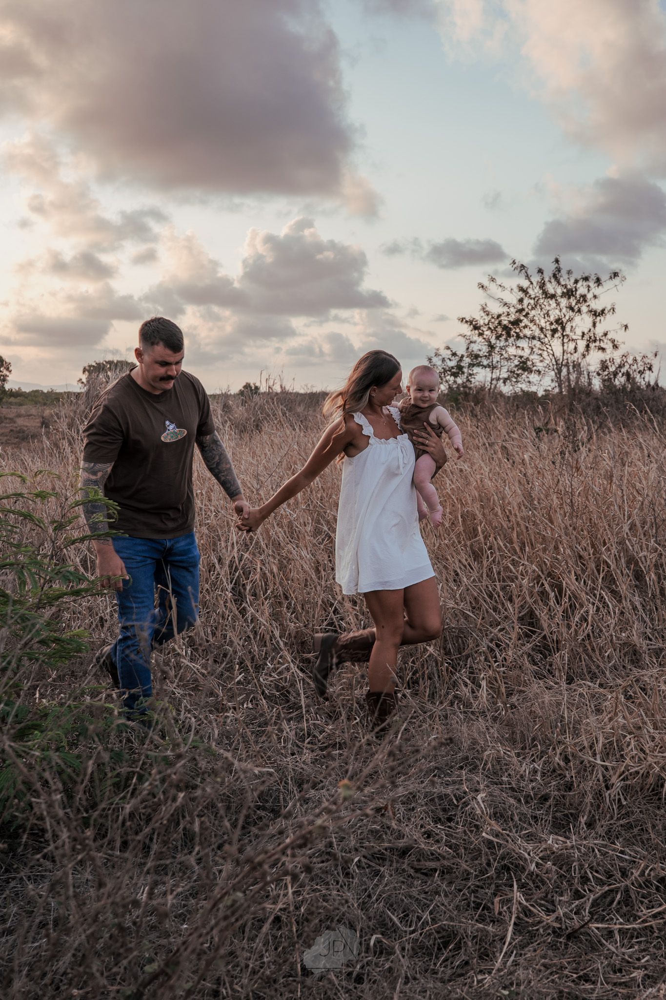 Two people dance and twirl together in a rustic field at dusk.