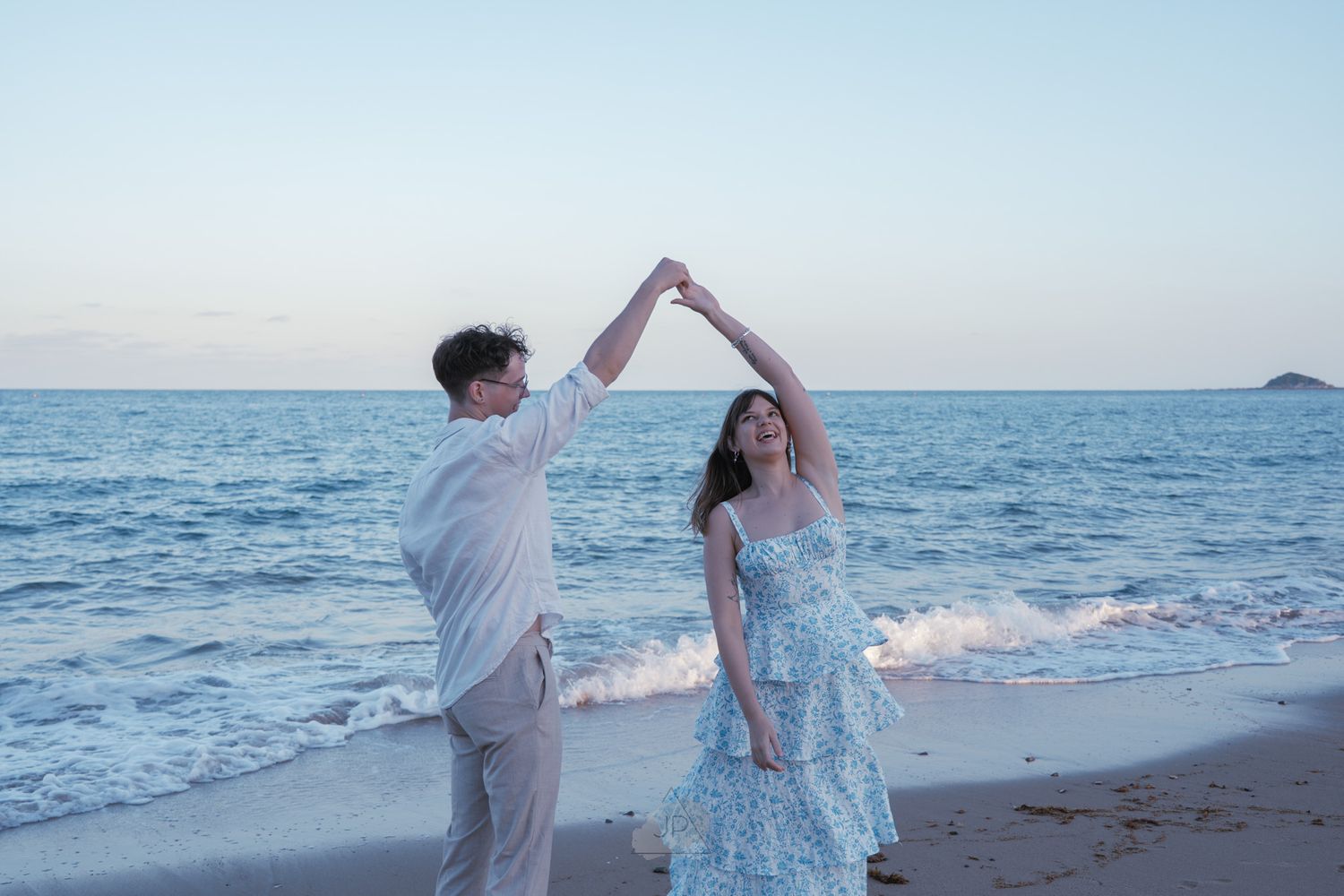 A couple dances together on a beach at sunset with gentle waves rolling in along the shoreline.
