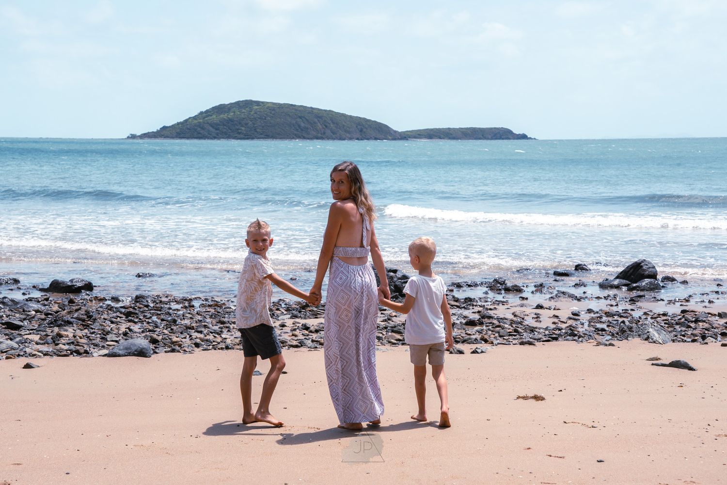 A family in white clothing sits together on a beach while looking out at the ocean and horizon.