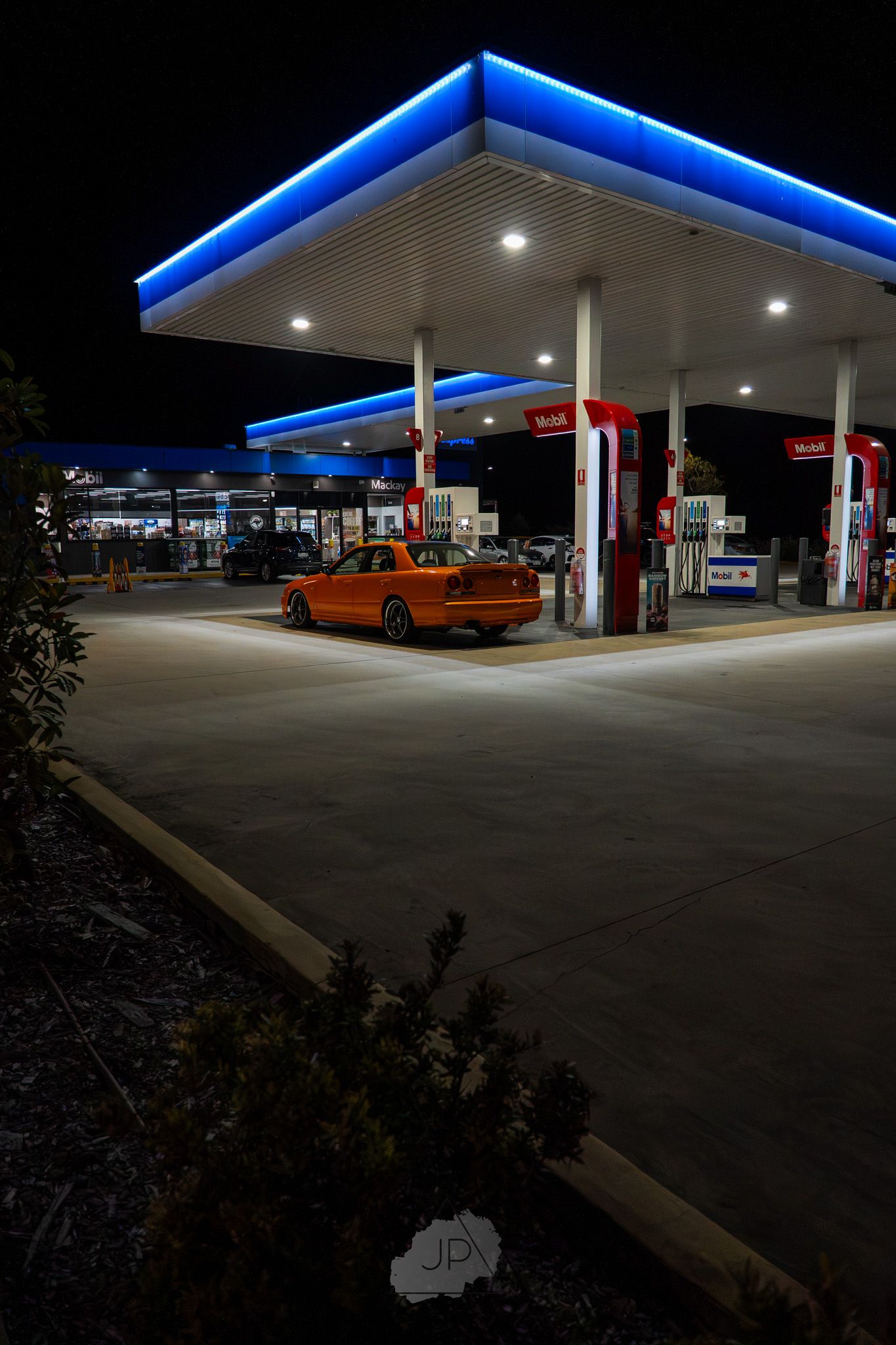 Modern gas station illuminated with bright blue LED lighting at night creates a striking architectural display.