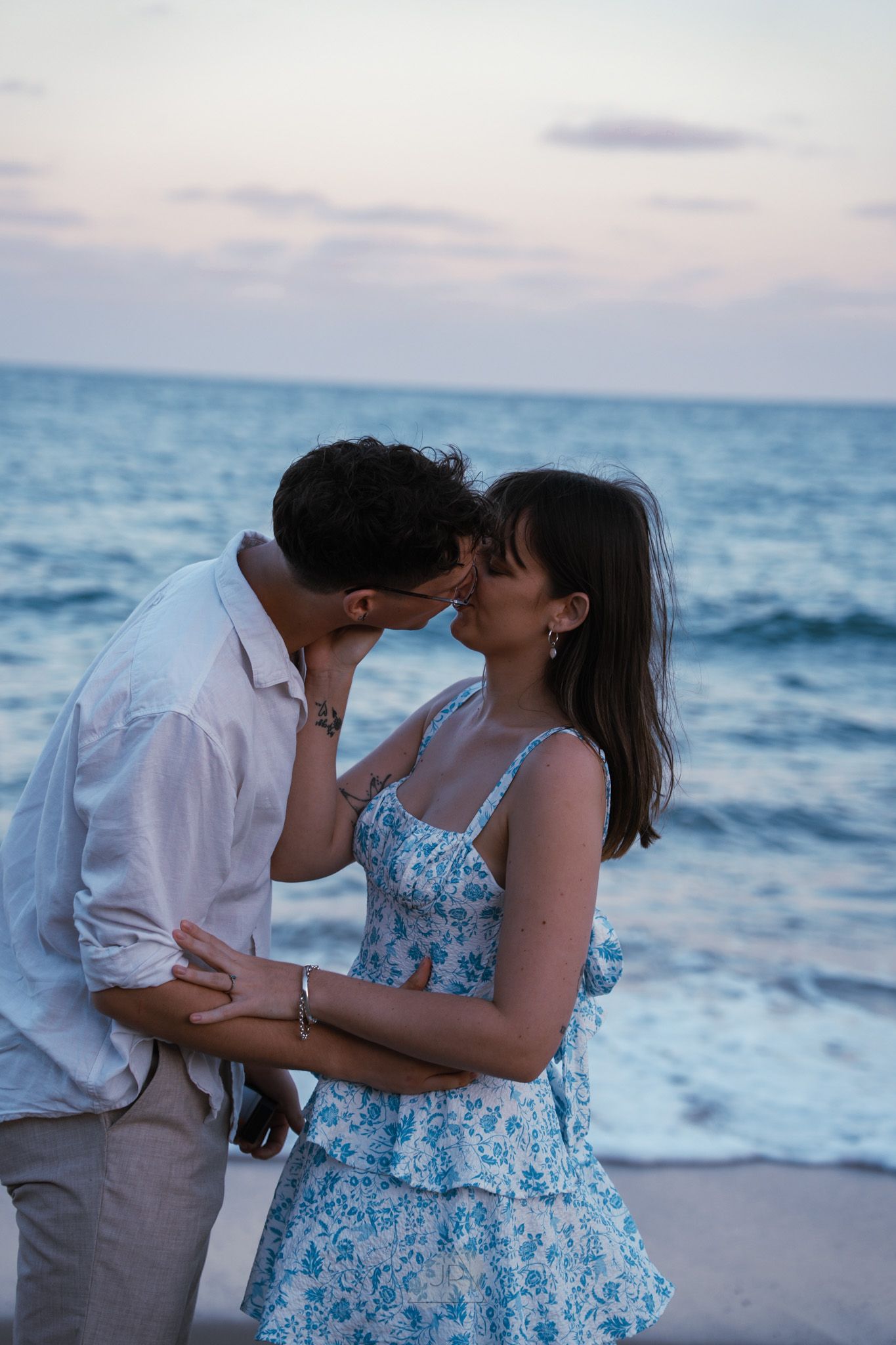 Romantic couple sharing intimate moments on a beach at sunset with ocean waves in the background.