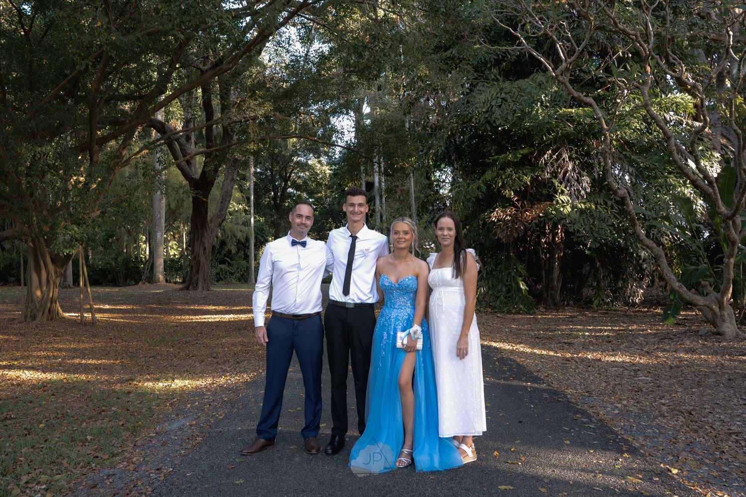 A group poses together in an outdoor wooded setting wearing formal attire in shades of blue and white.