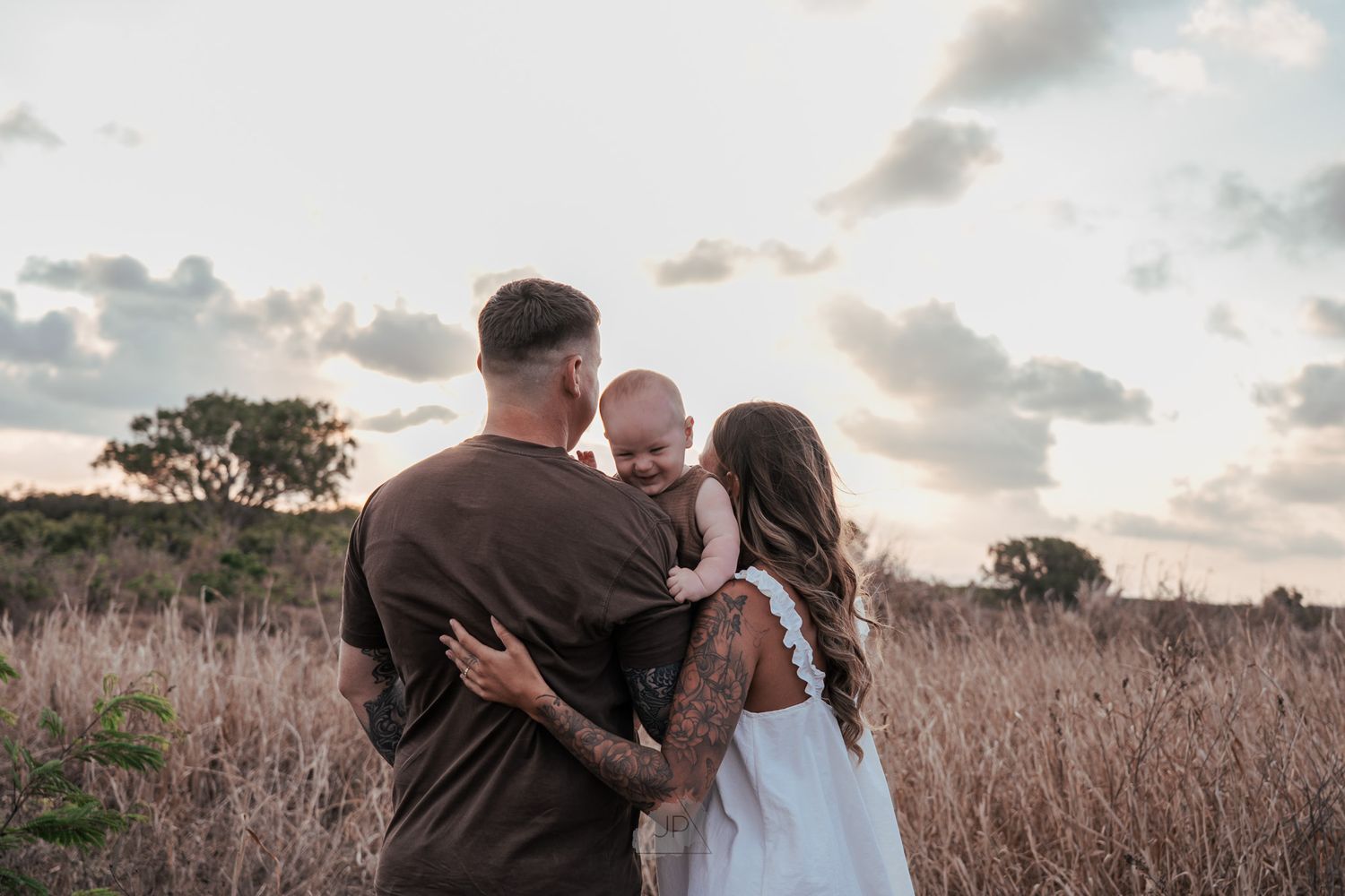 A couple embraces in a golden field at sunset during a romantic photoshoot.