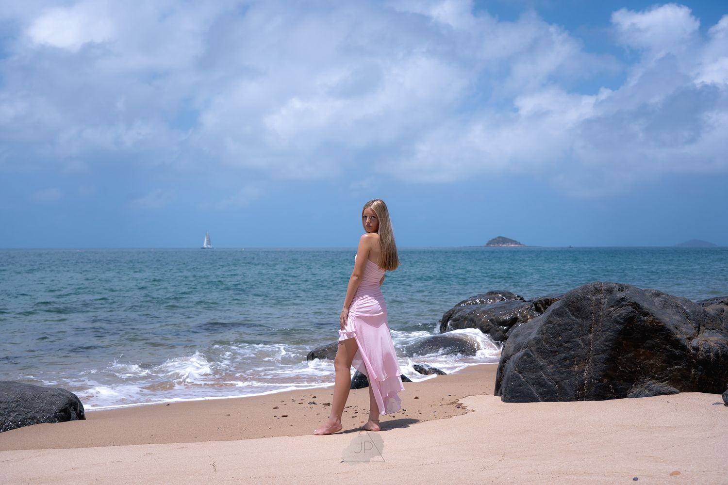 A panoramic beach scene with crashing waves, rocky outcrops and turquoise waters under a bright blue sky.