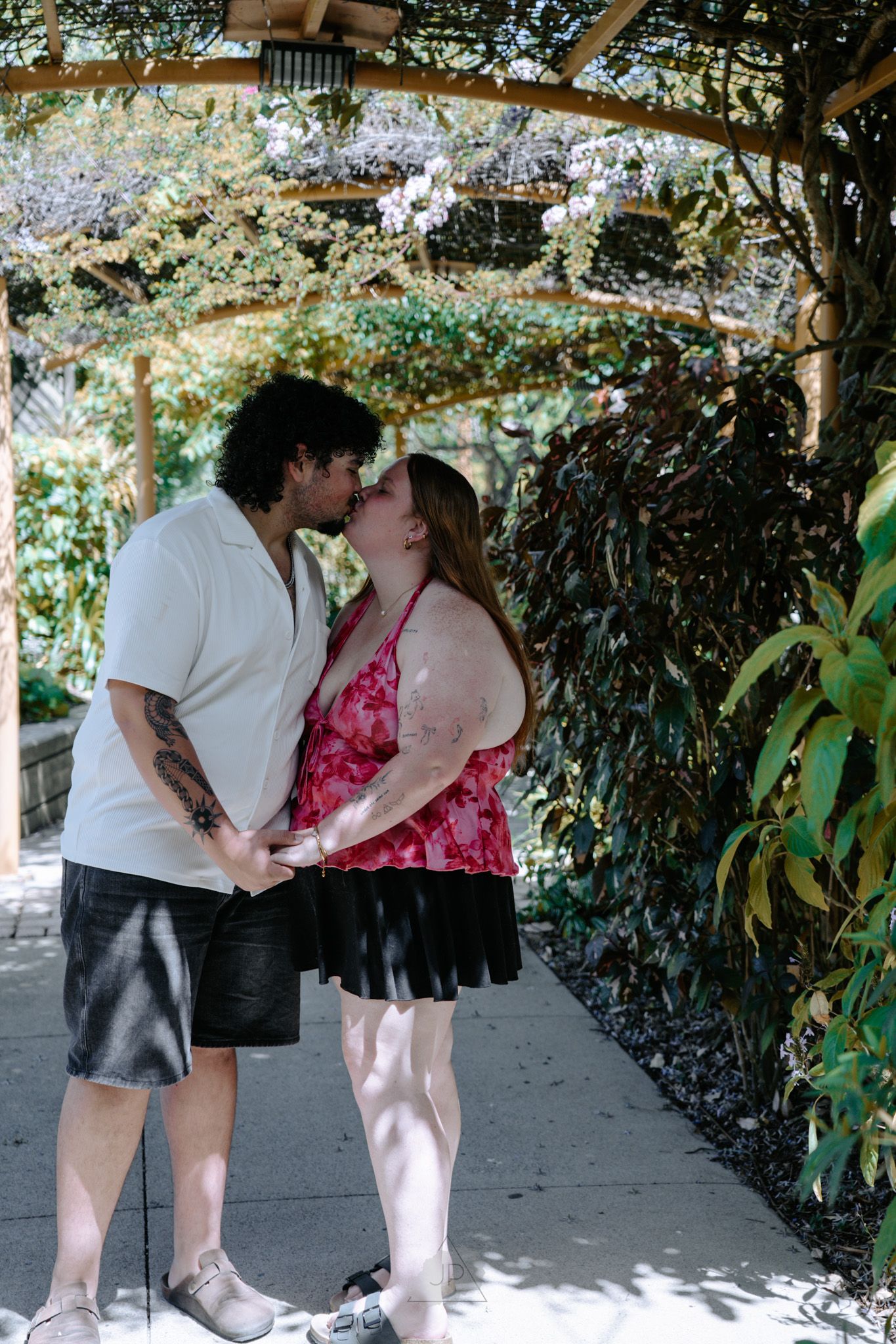 A couple shares an intimate moment under a leafy garden arbor in a sequence of four connected photos.
