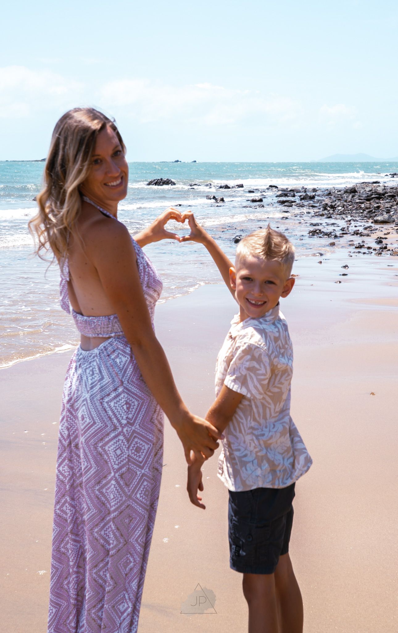 A parent and child share a joyful moment together while playing on a sunny beach with ocean waves in the background.