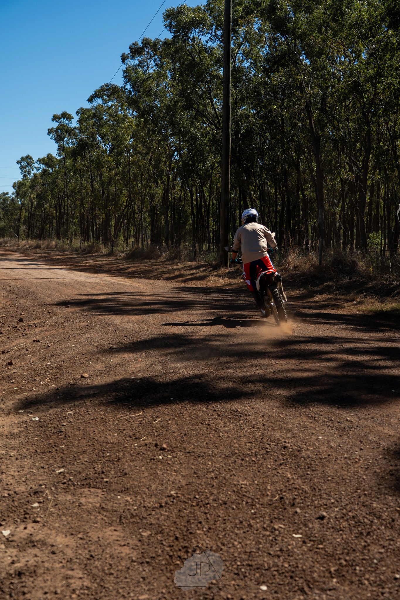 Motorcyclists riding on a dusty dirt track through Australian bushland surrounded by tall eucalyptus trees.