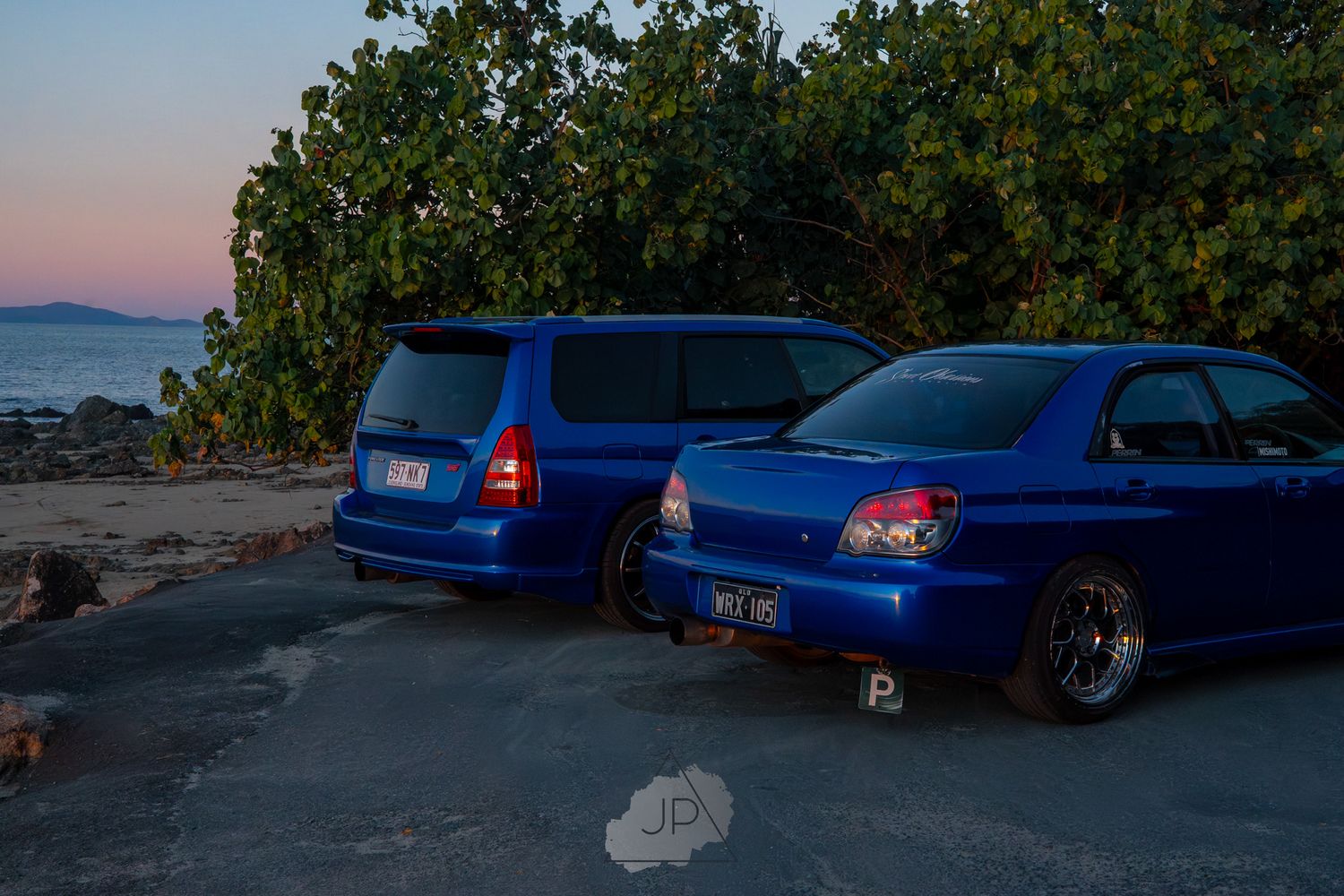 A series of blue Subaru WRX sports cars lined up against a scenic mountain backdrop during sunset.