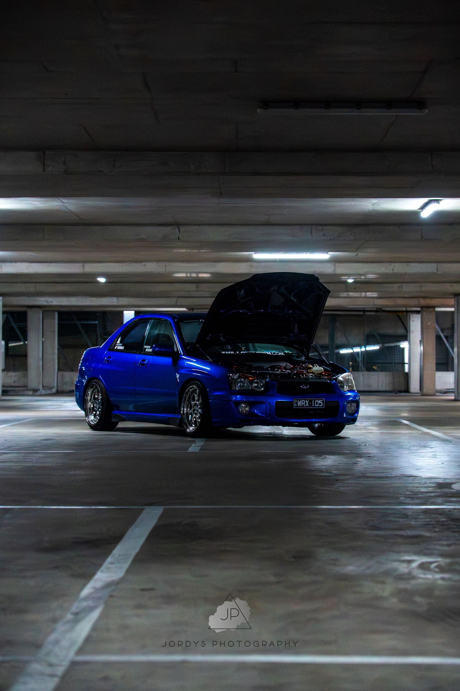 Dark parking garage with a blue BMW M3 parked under dim lighting creating a moody automotive atmosphere.