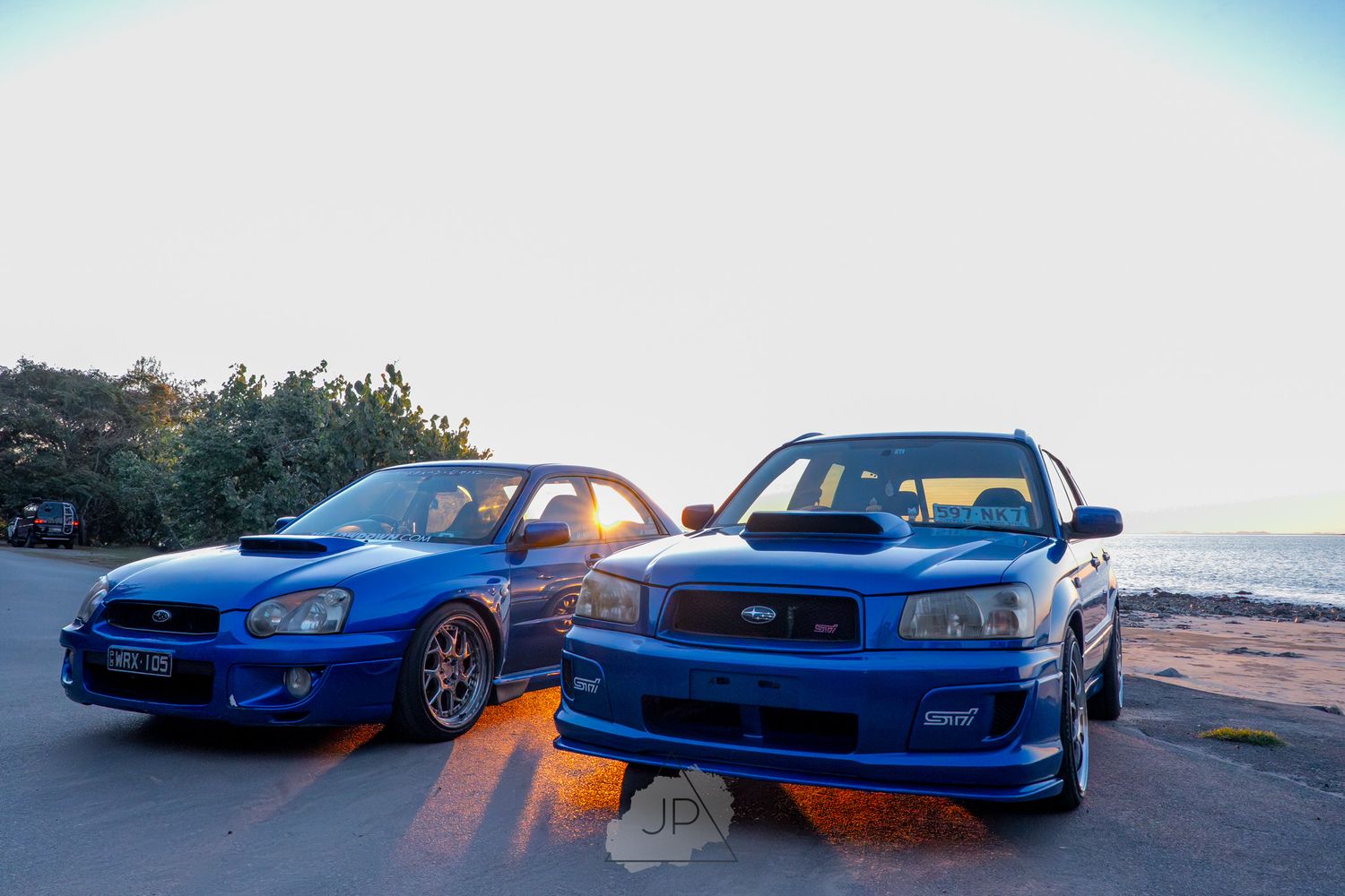 Five blue Subaru WRX sports cars parked in a row during sunset with orange sky in the background.