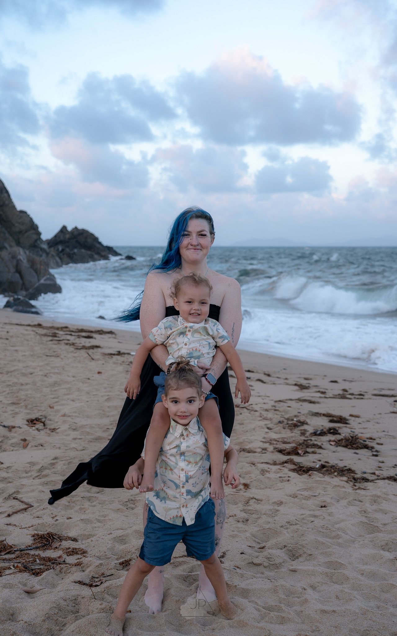 A family plays together on a cloudy beach with crashing waves and rocky cliffs in the background.