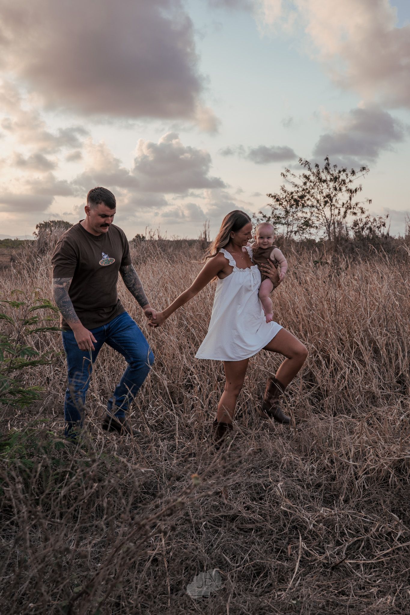 A couple shares a romantic dance in a field of brown grass during golden hour.