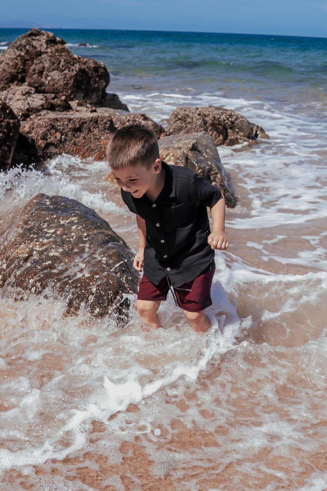 A sequence of photos showing a child playing and splashing in the waves along a rocky beach shoreline.