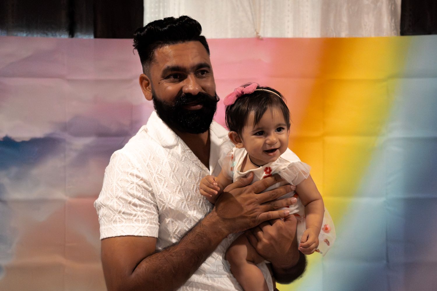 A person holds a smiling baby in front of a colorful rainbow backdrop during a photo session.
