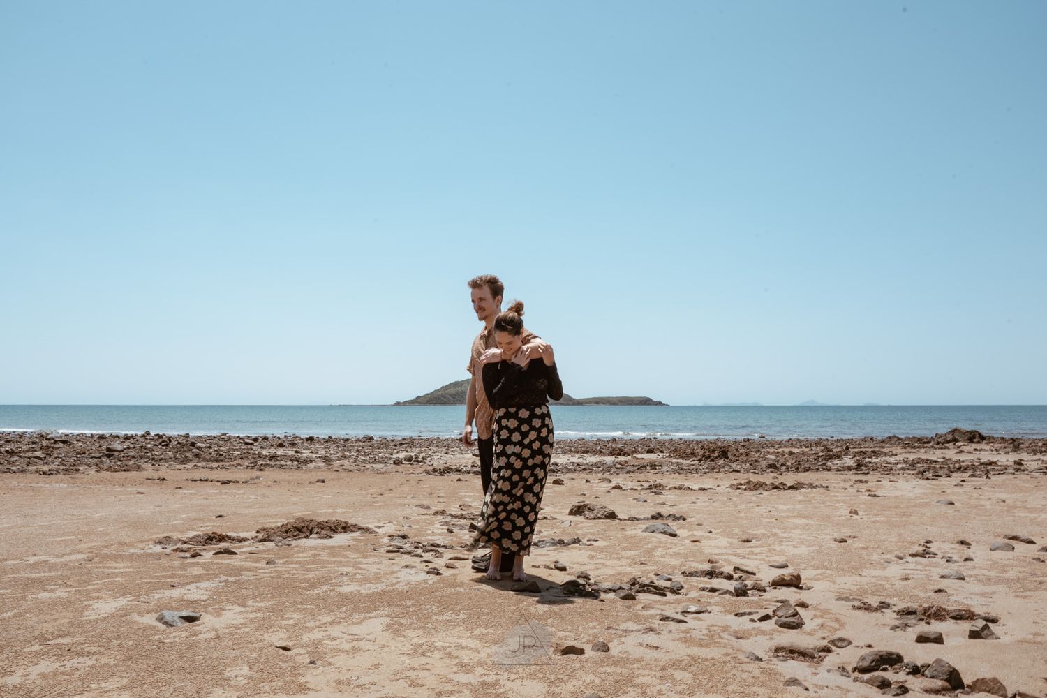 Panoramic sequence of someone in a leopard print dress walking along a vast empty beach on a sunny day.