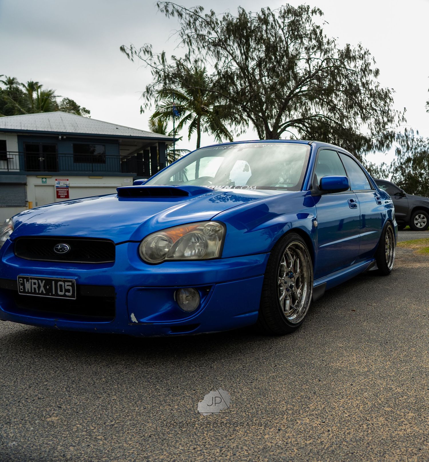 Modified Subaru Impreza WRX in metallic blue showcasing custom wheels and lowered suspension on gravel road.