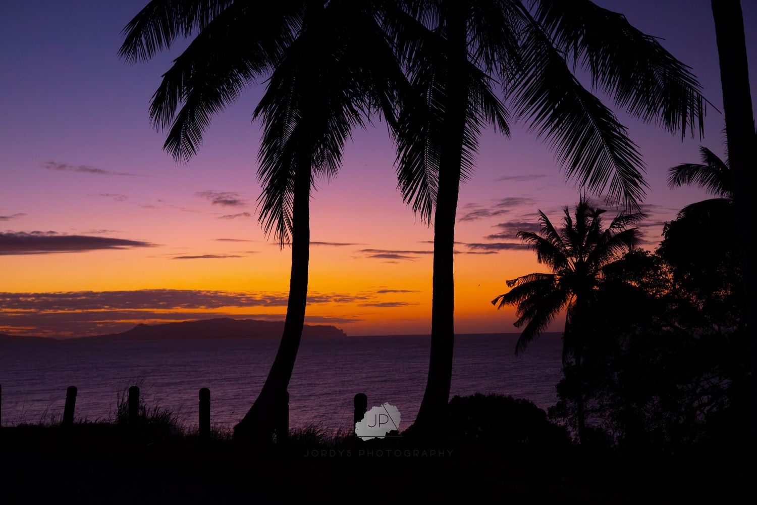Silhouettes of palm trees against a vibrant orange and purple tropical sunset sky over the ocean.