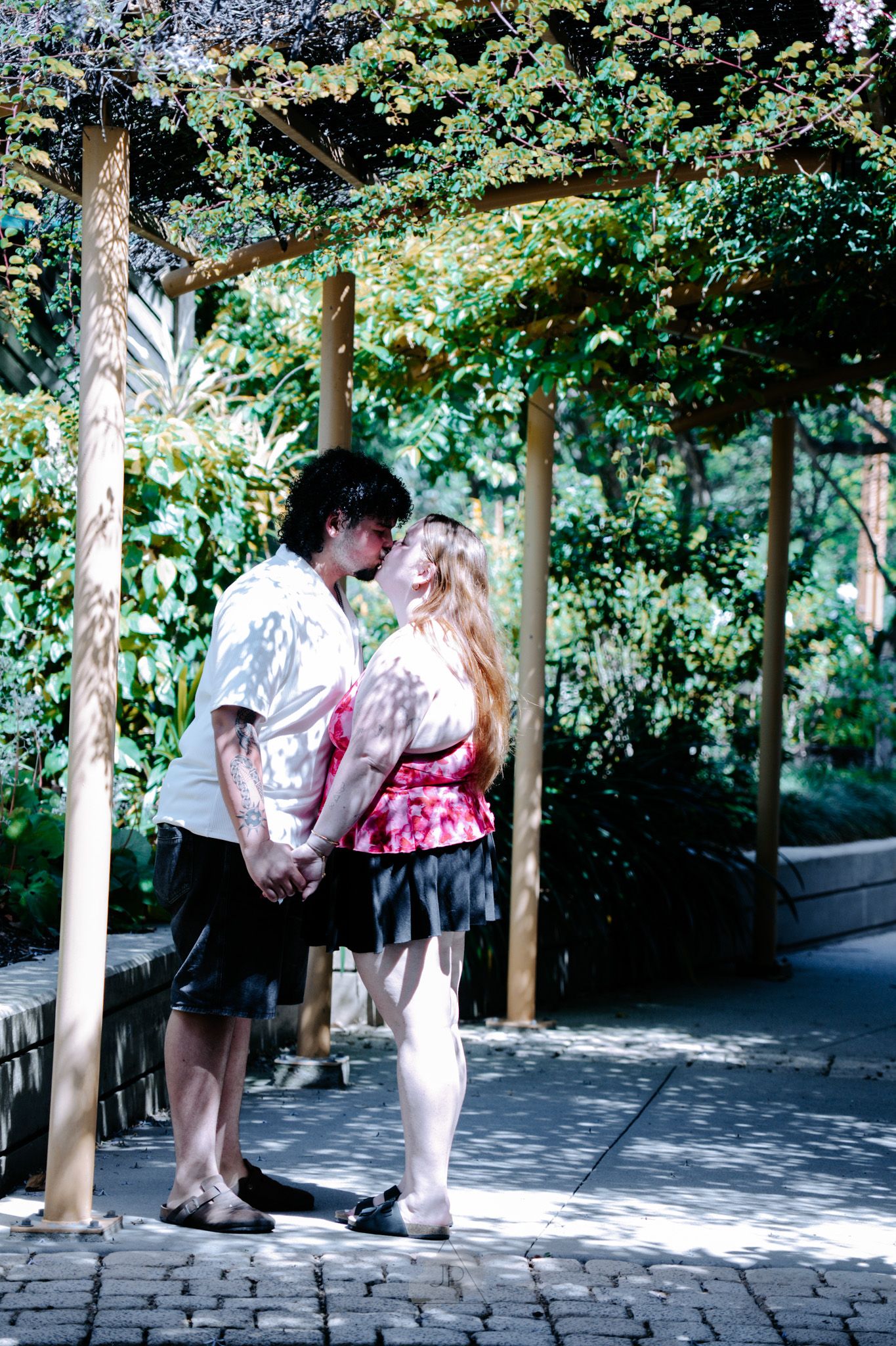 A sequence of images showing a couple in casual attire sharing a romantic moment on a tree-lined stone path.