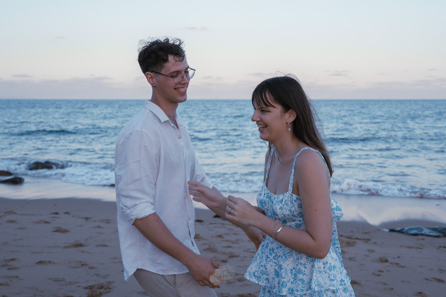 A happy couple shares a romantic moment on the beach at sunset with the ocean waves in the background.