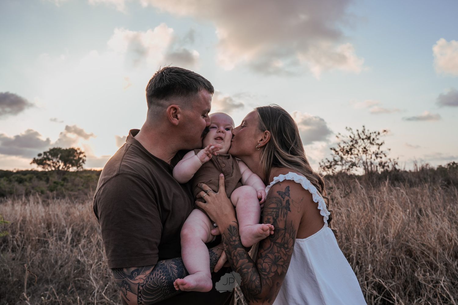 A family shares a tender moment together in a field at sunset with warm golden light and tall grass surrounding them.
