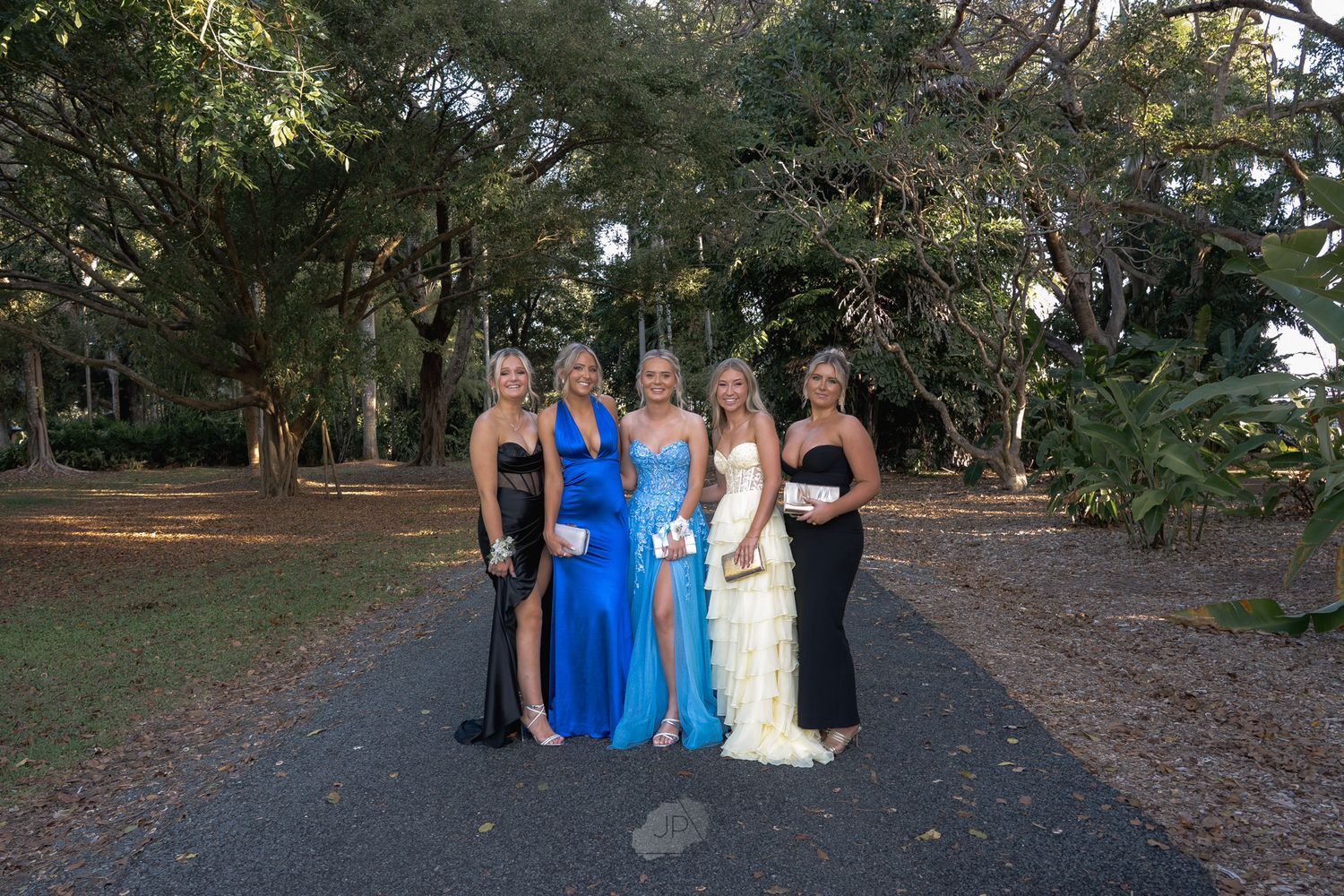 A group of people in formal attire pose together outdoors in a garden setting for a special occasion.