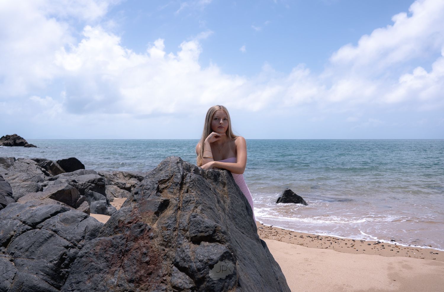 A person stands on rocky coastal cliffs overlooking turquoise ocean waters on a sunny day.