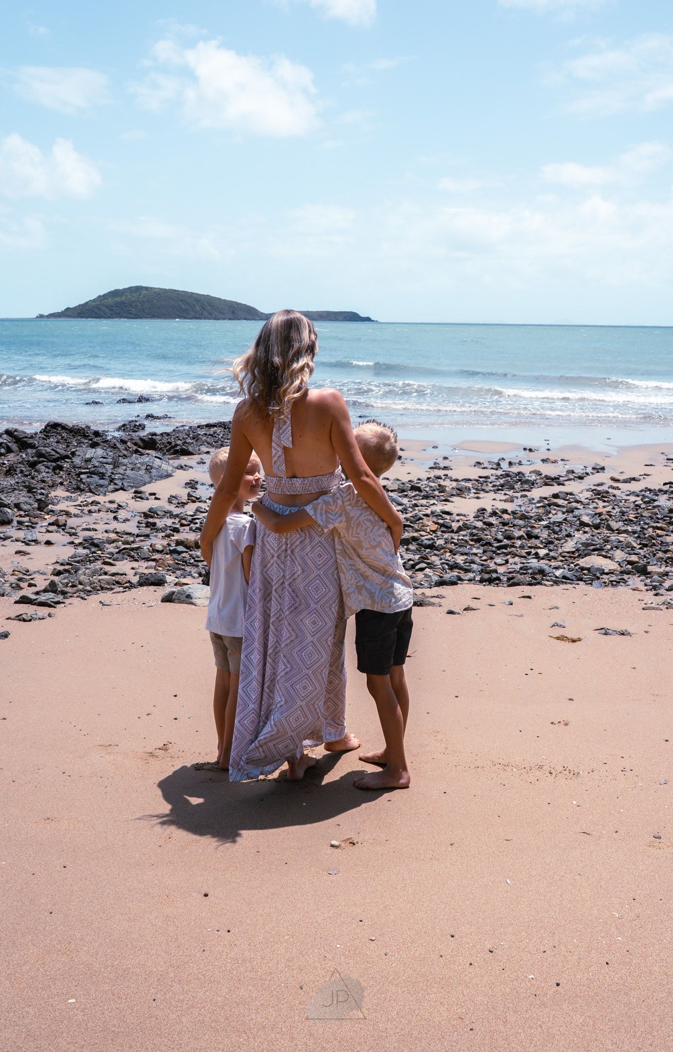 Two people explore a rocky beach shoreline with turquoise ocean waters and blue skies in the background.