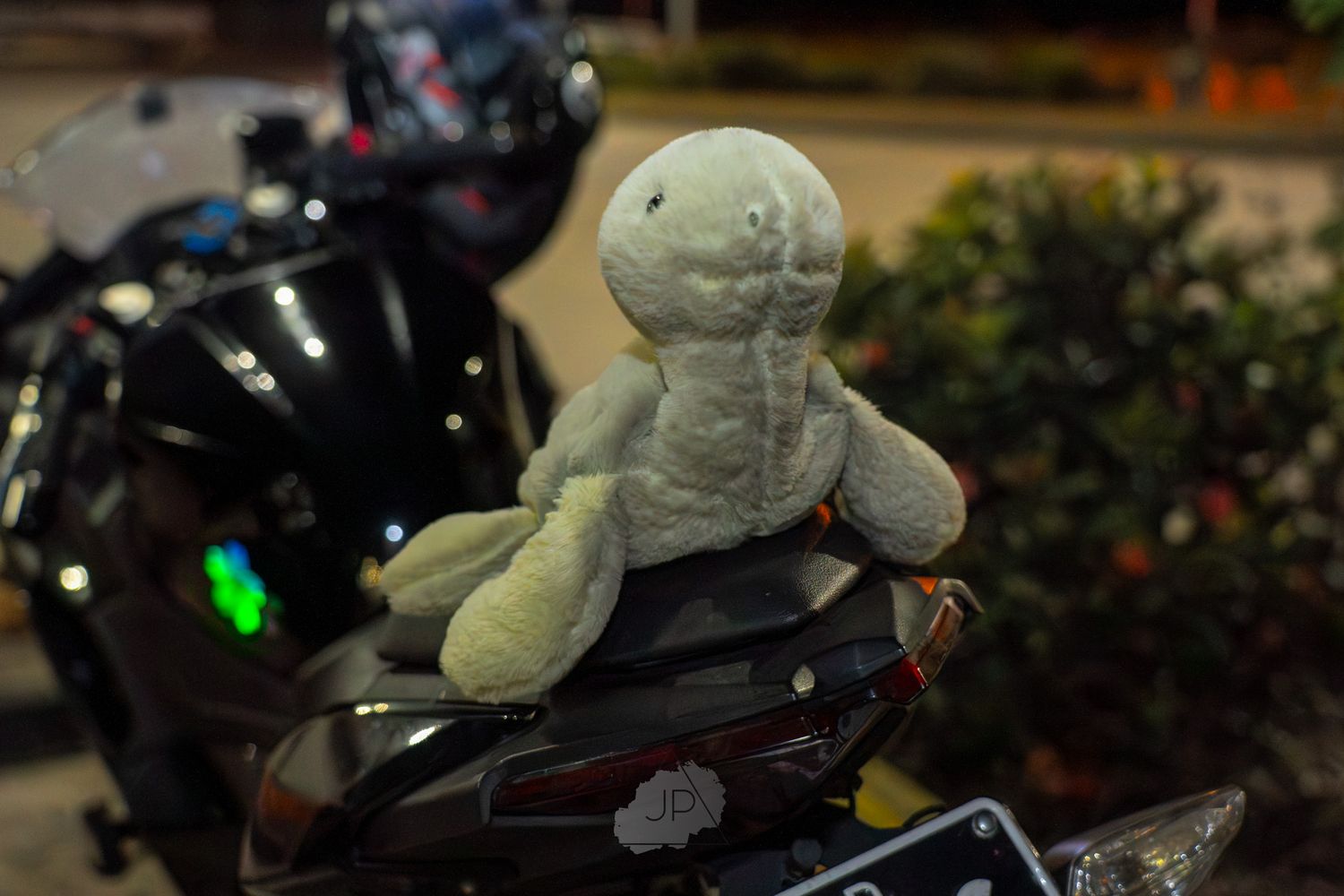 A small plush toy sits on the seat of a parked motorcycle at night.