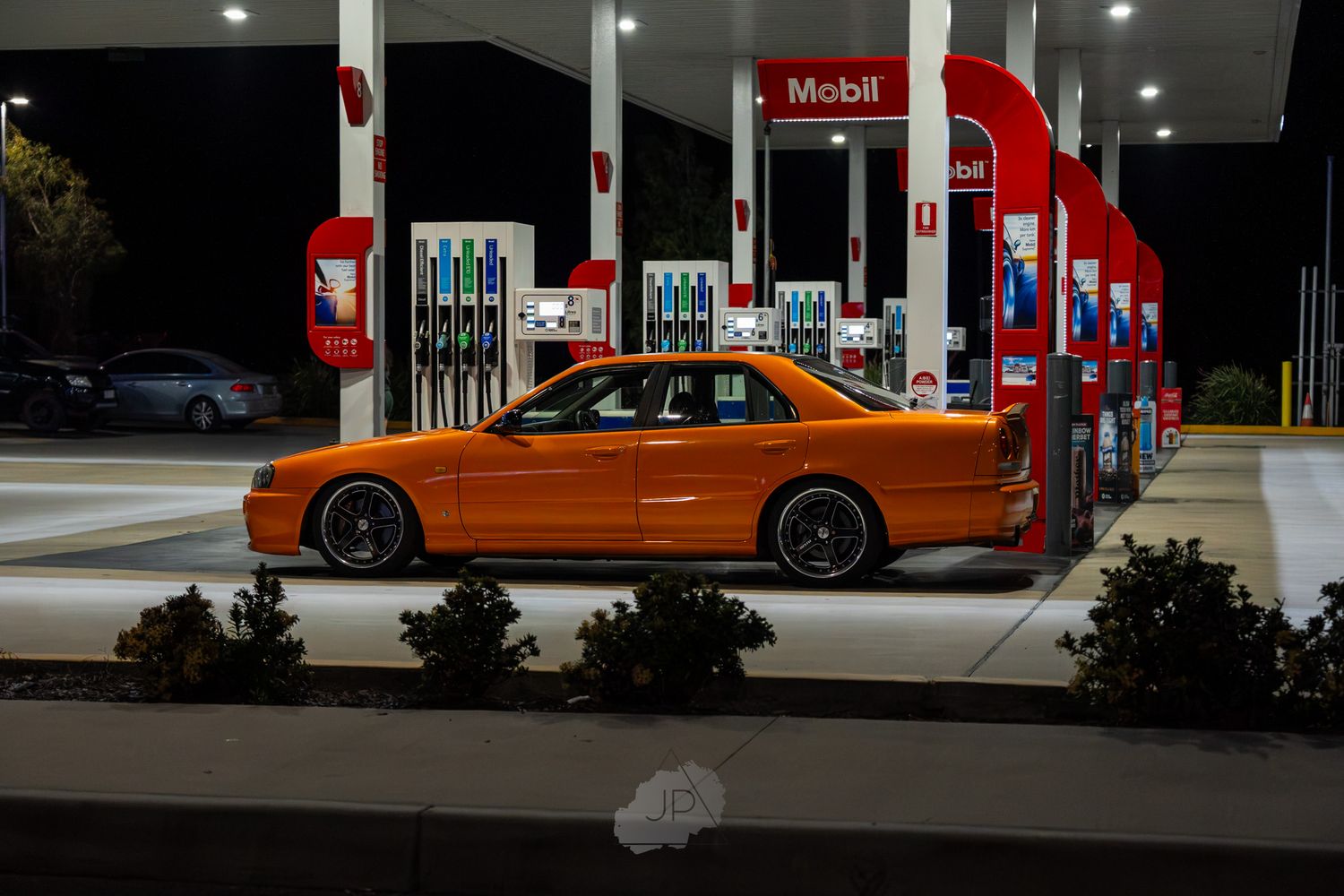 Illuminated Mobil gas station with orange performance car visible in the darkness.