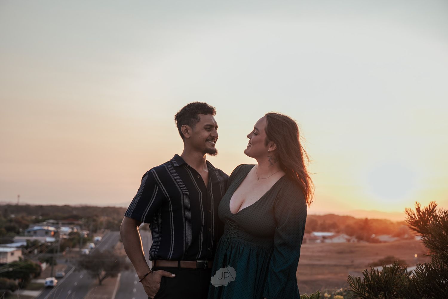 Romantic couple silhouetted against golden sunset sky on rooftop with cityscape in background.
