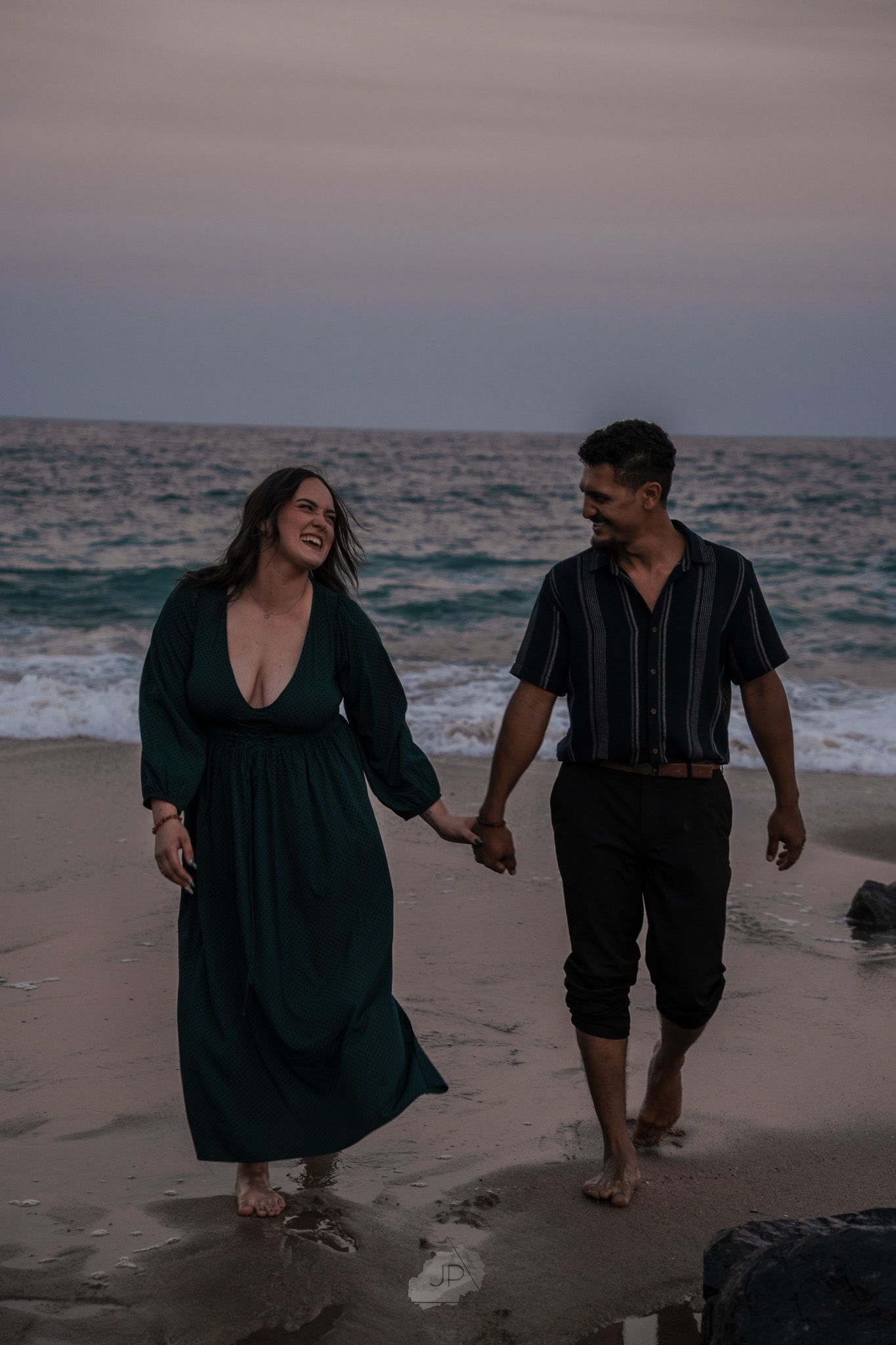 A couple walks playfully along the beach at sunset, splashing and enjoying a romantic moment by the ocean waves.